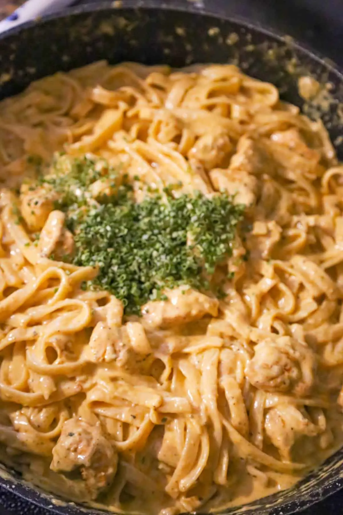 chopped chives on top of cajun chicken alfredo in a saute pan