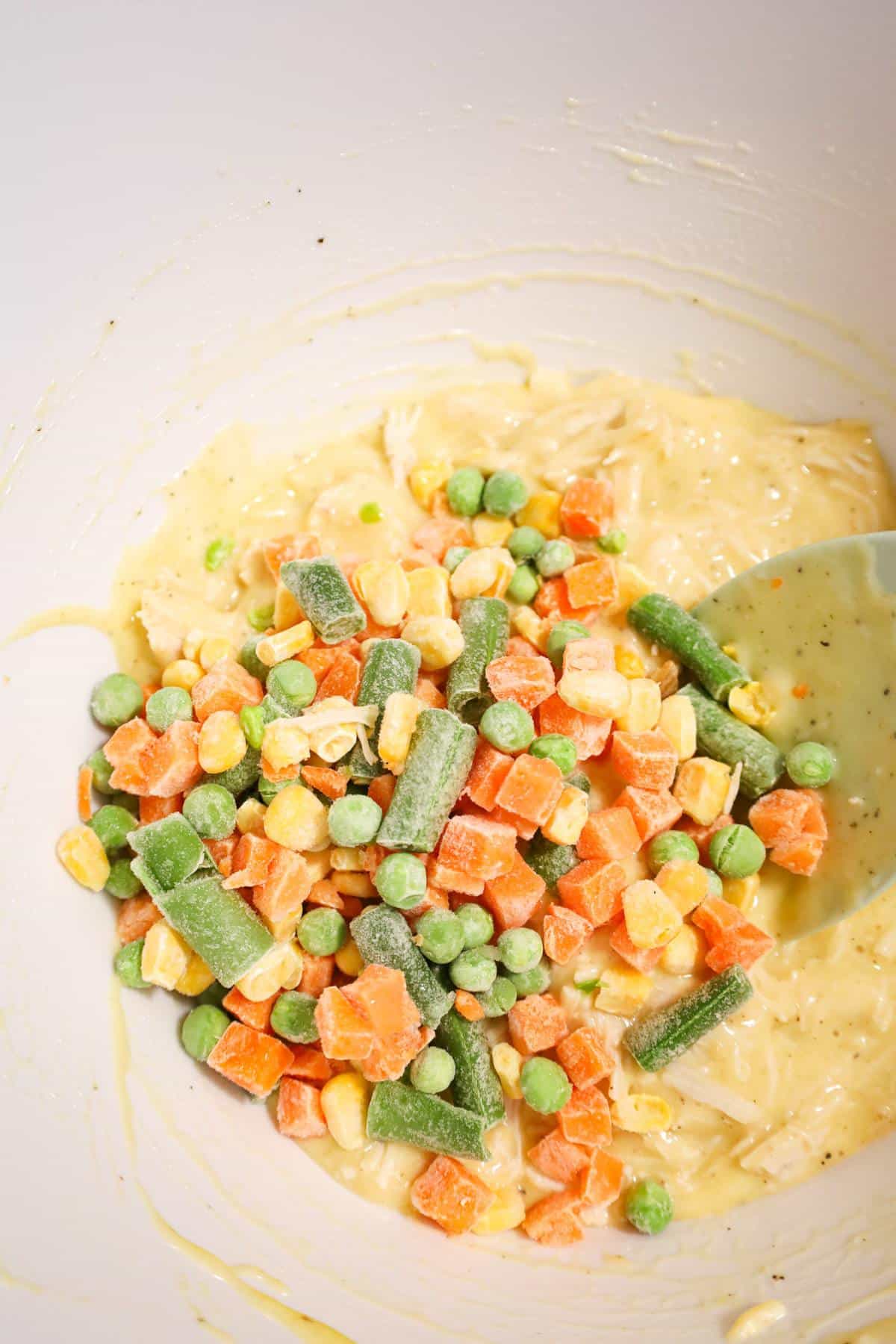 frozen mixed veggies on top of creamy chicken mixture in a mixing bowl