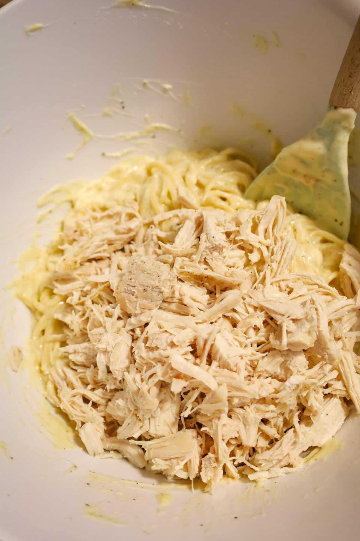 shredded chicken on top of spaghetti in a mixing bowl