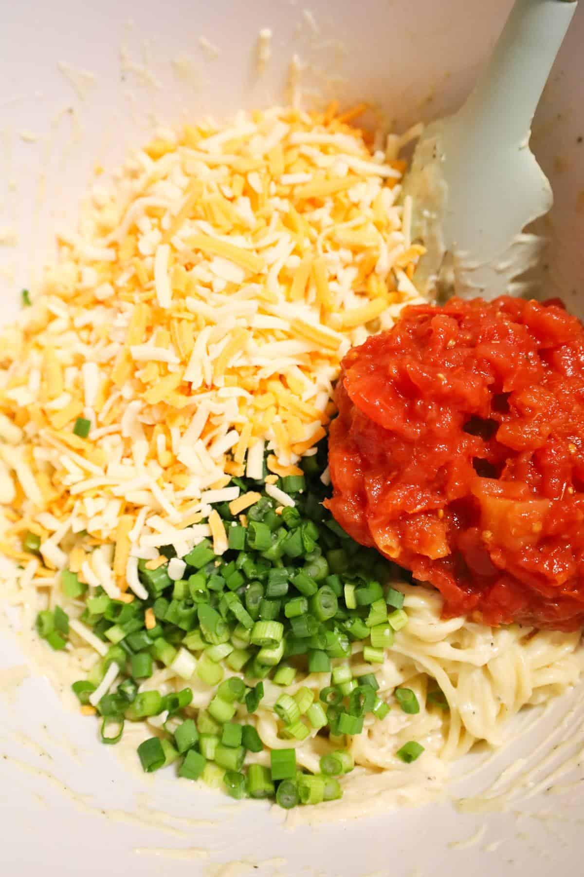 shredded cheese, chopped green onions and rotel on top of spaghetti in a mixing bowl