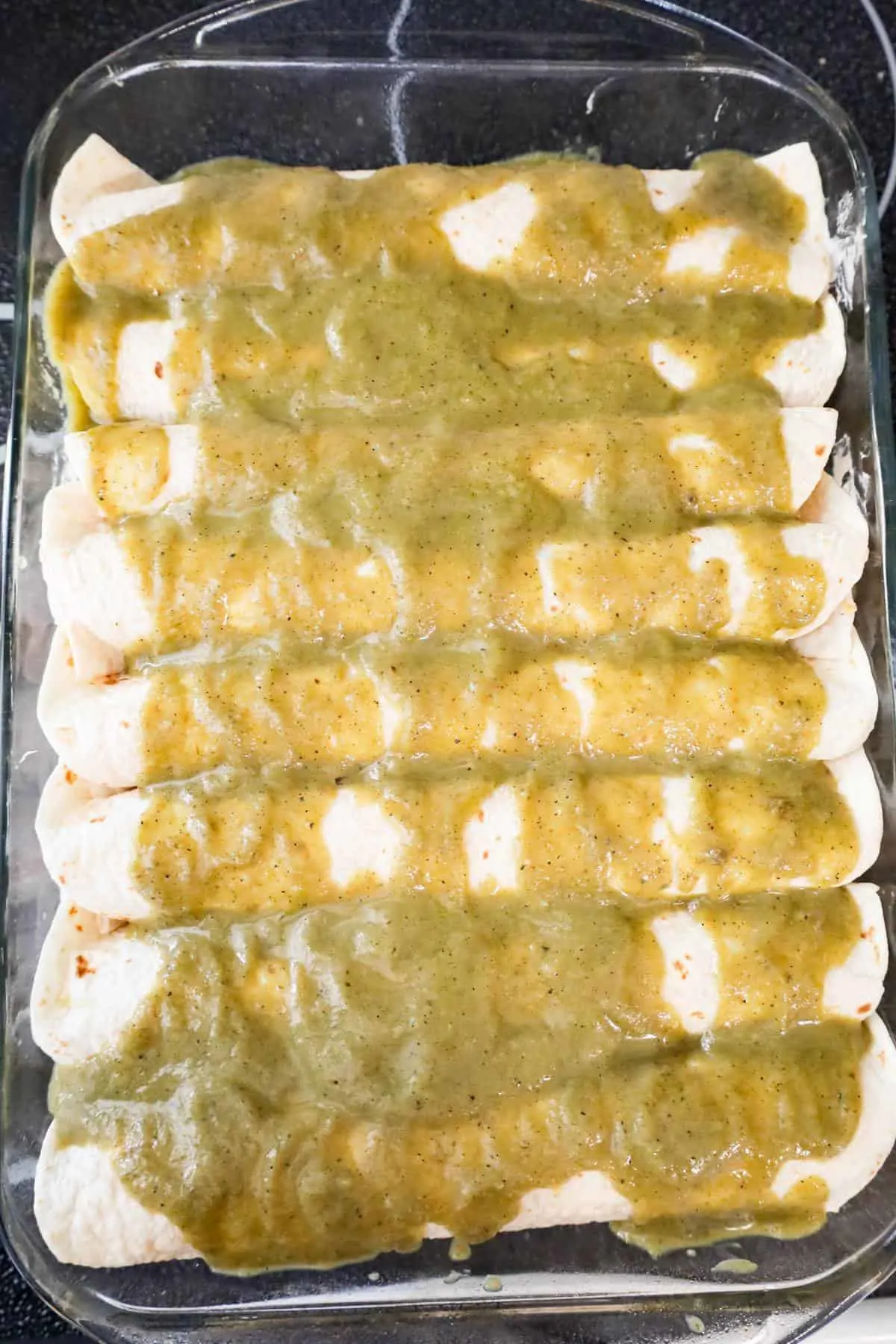 green enchilada sauce on top of rolled tortillas in a baking dish