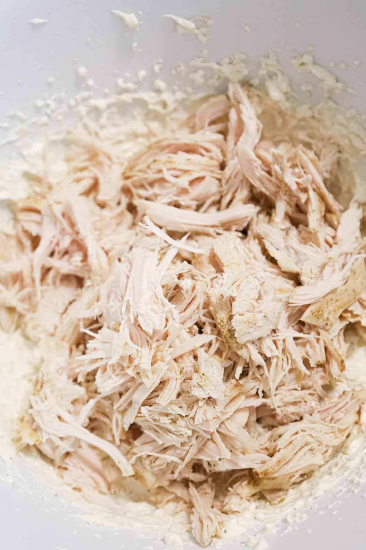 shredded chicken on top of cream cheese and sour cream mixture in a mixing bowl