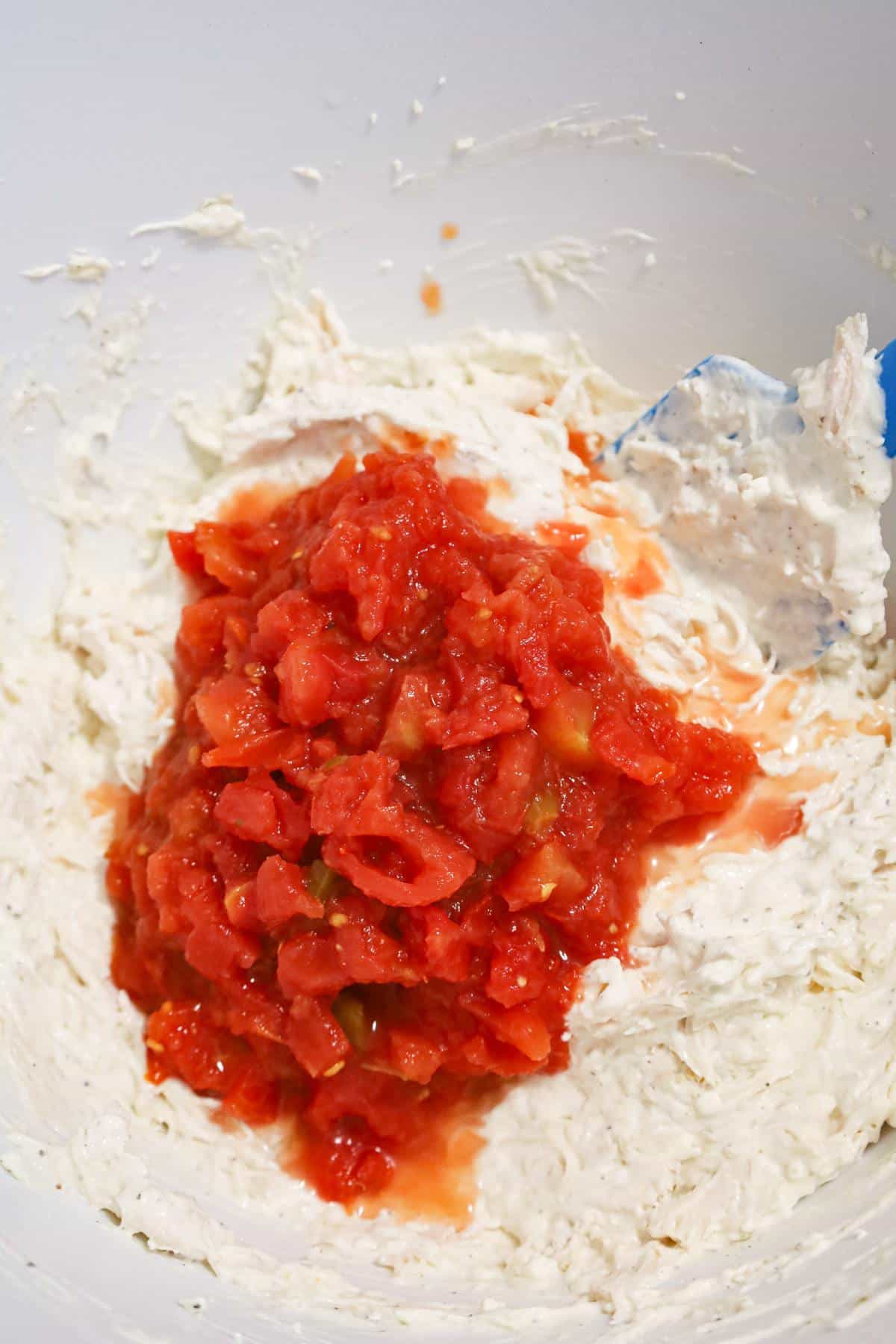 Rotel diced tomatoes on top of creamy chicken mixture in a mixing bowl