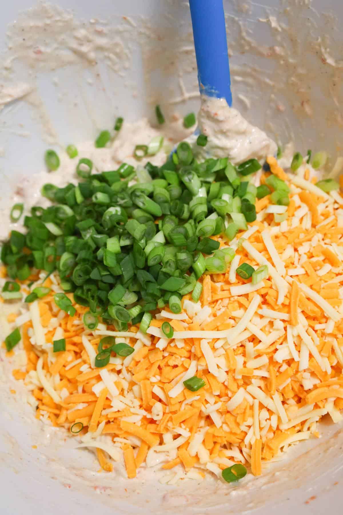 chopped green onions and shredded cheese on top of a cream cheese chicken mixture in a mixing bowl