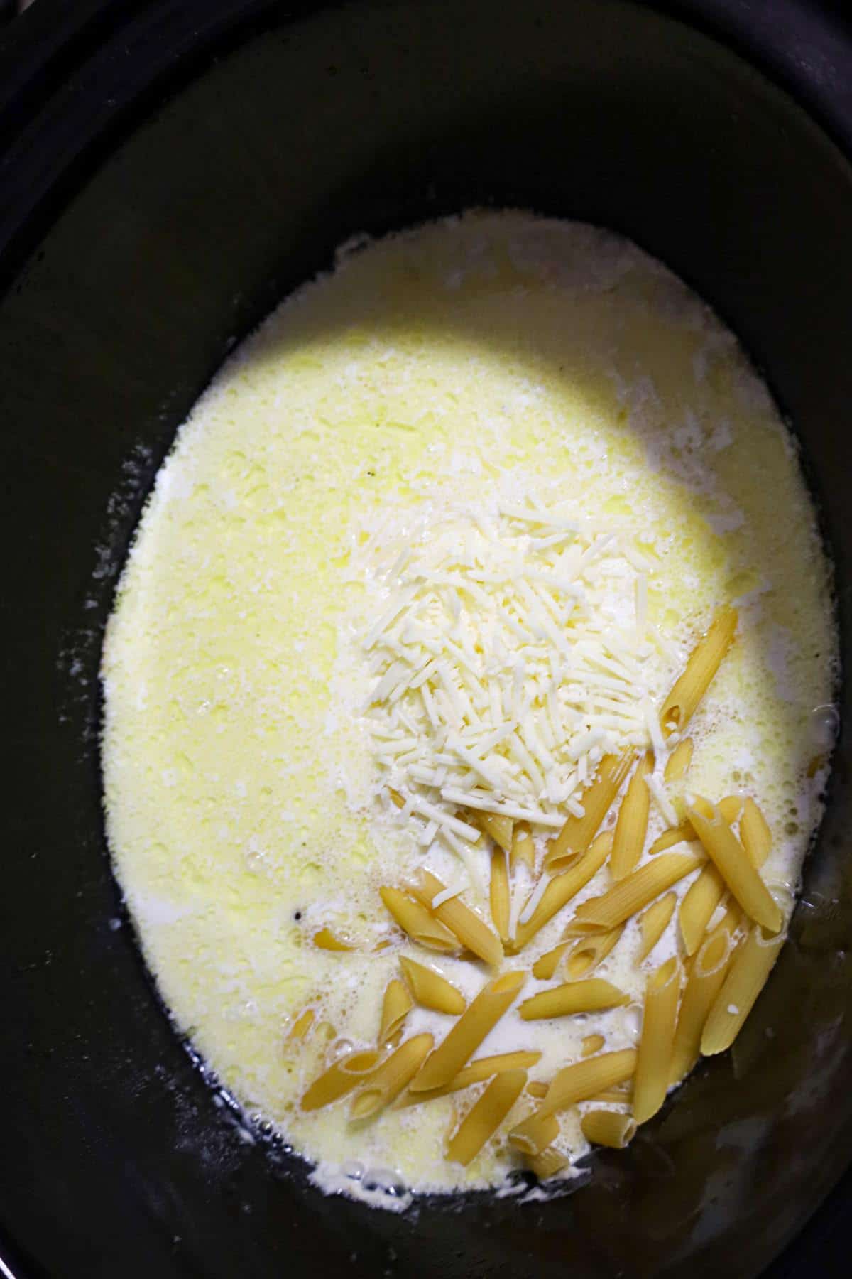 penne noodles and shredded parmesan cheese added to alfredo sauce in a crock pot