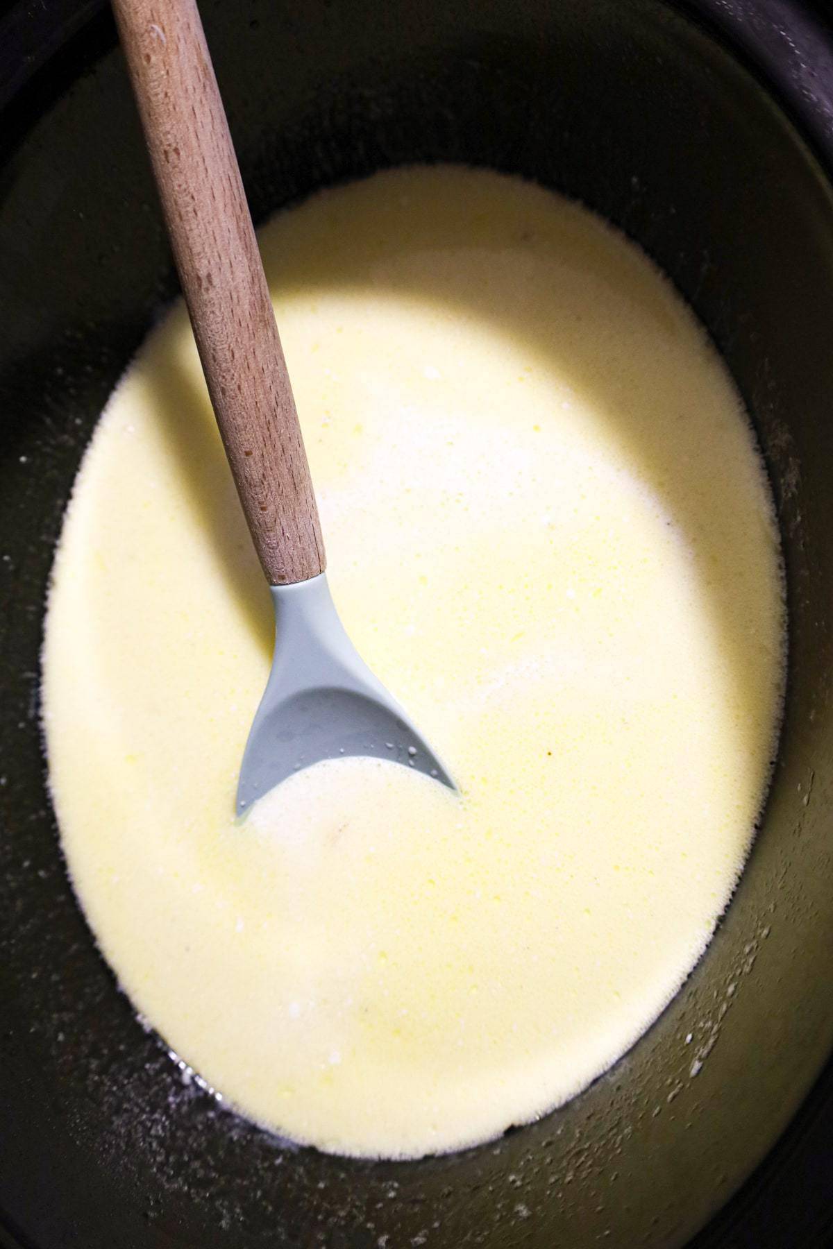 stirring penne noodles into alfredo sauce in a crock pot