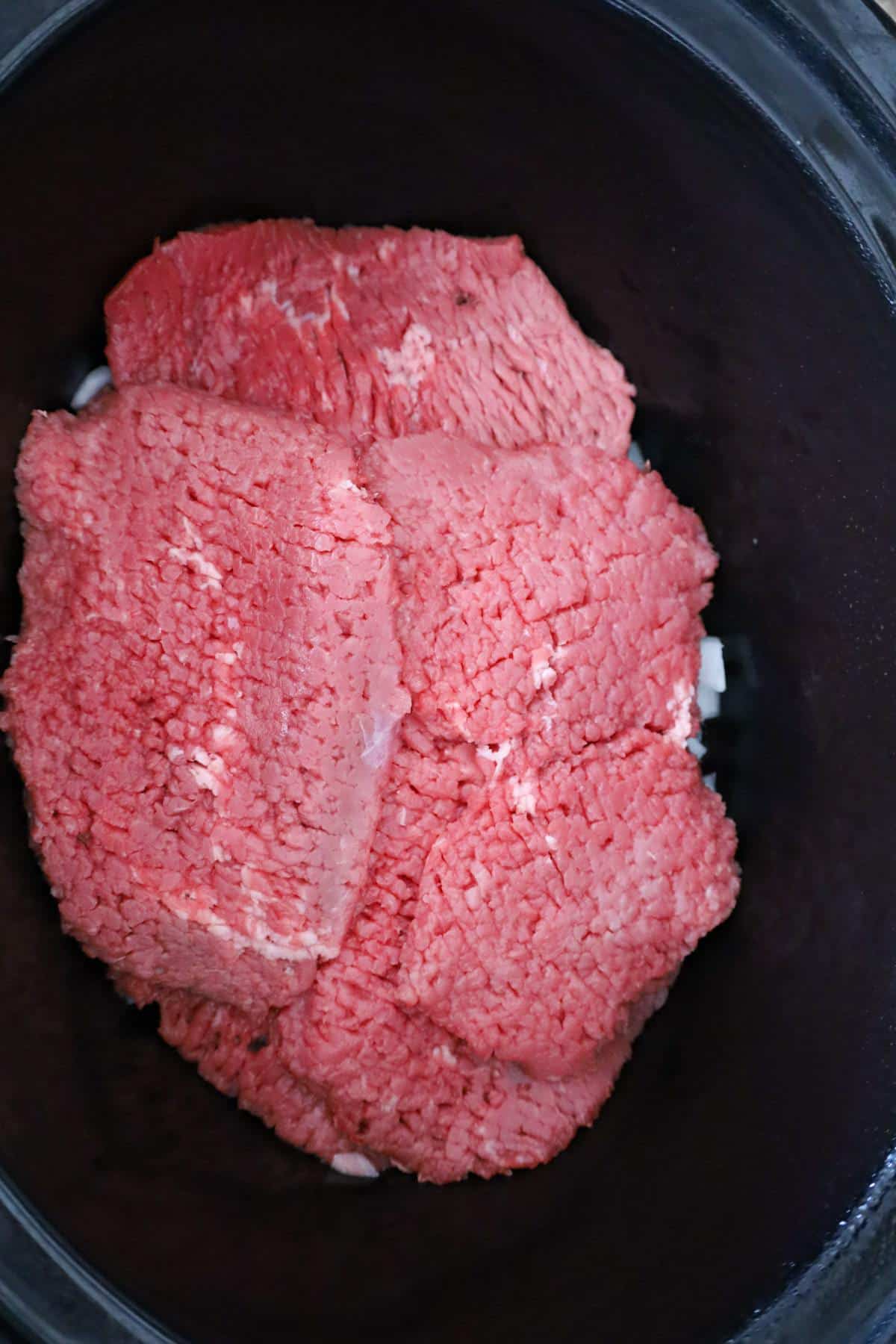 cube steaks on top of diced onions in a Crock Pot