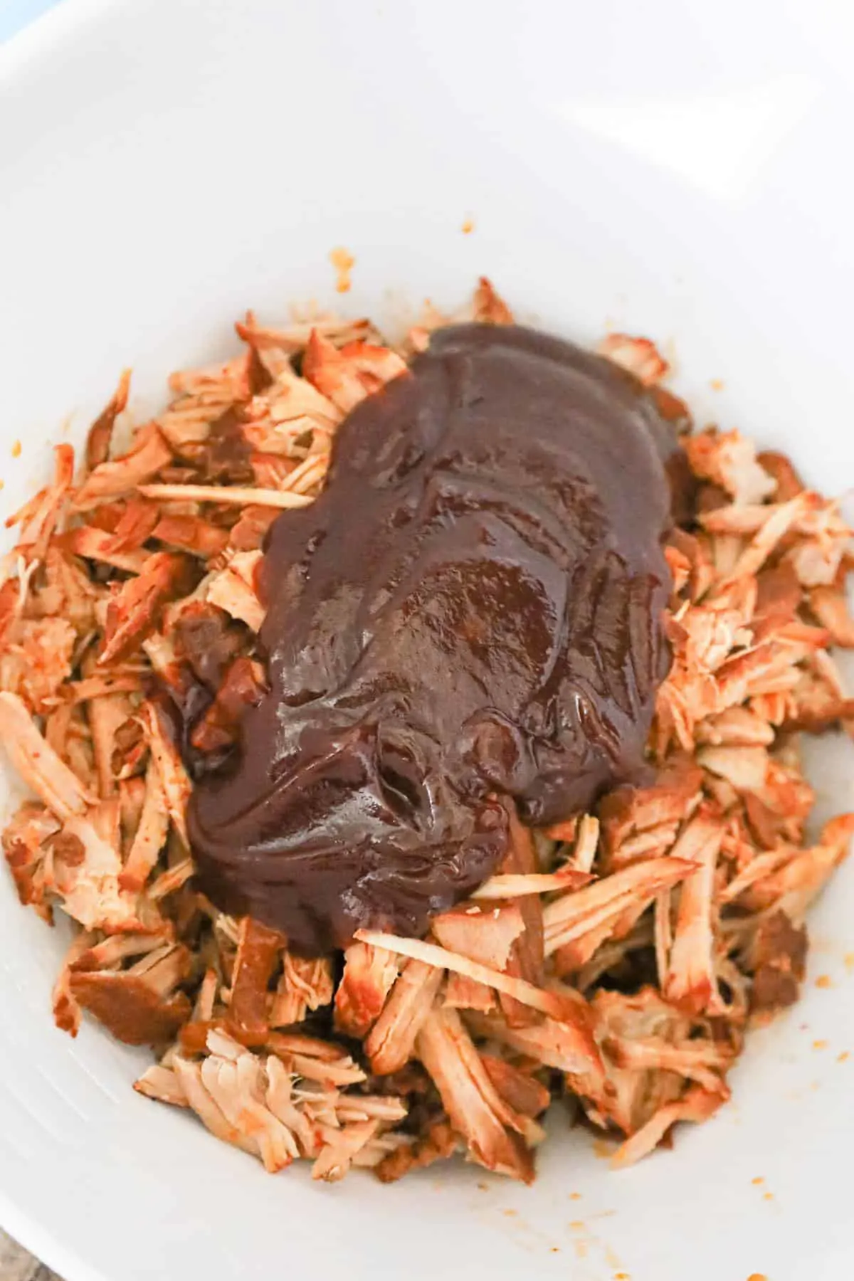 barbecue sauce on top of shredded pork in a mixing bowl