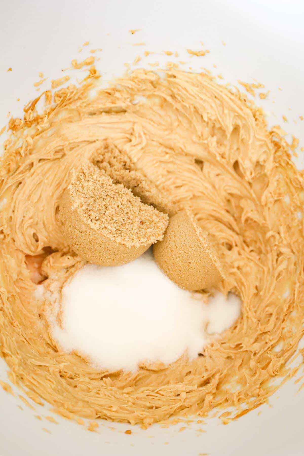 brown sugar and white sugar on top of creamy peanut butter mixture in a mixing bowl
