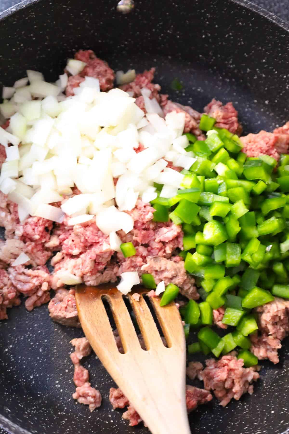 diced onions and diced green peppers on top of ground beef in a saute pan