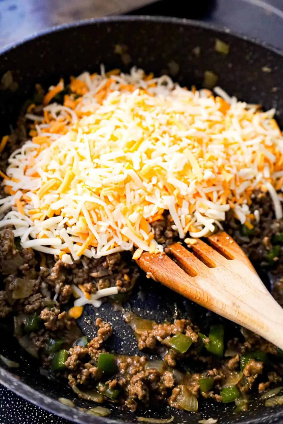 shredded mozzarella and cheddar cheese on top of ground beef mixture in a saute pan
