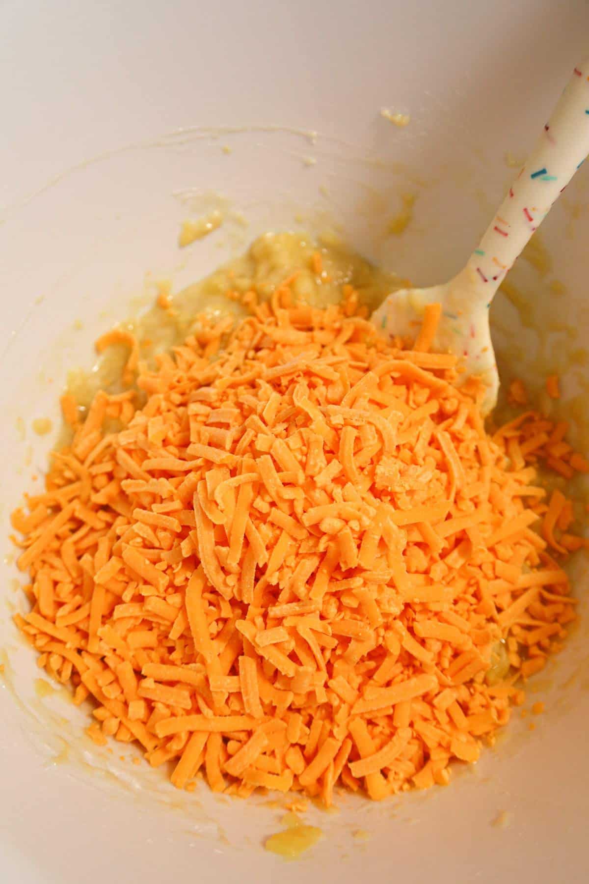shredded cheddar cheese on top of pineapple mixture in a mixing bowl