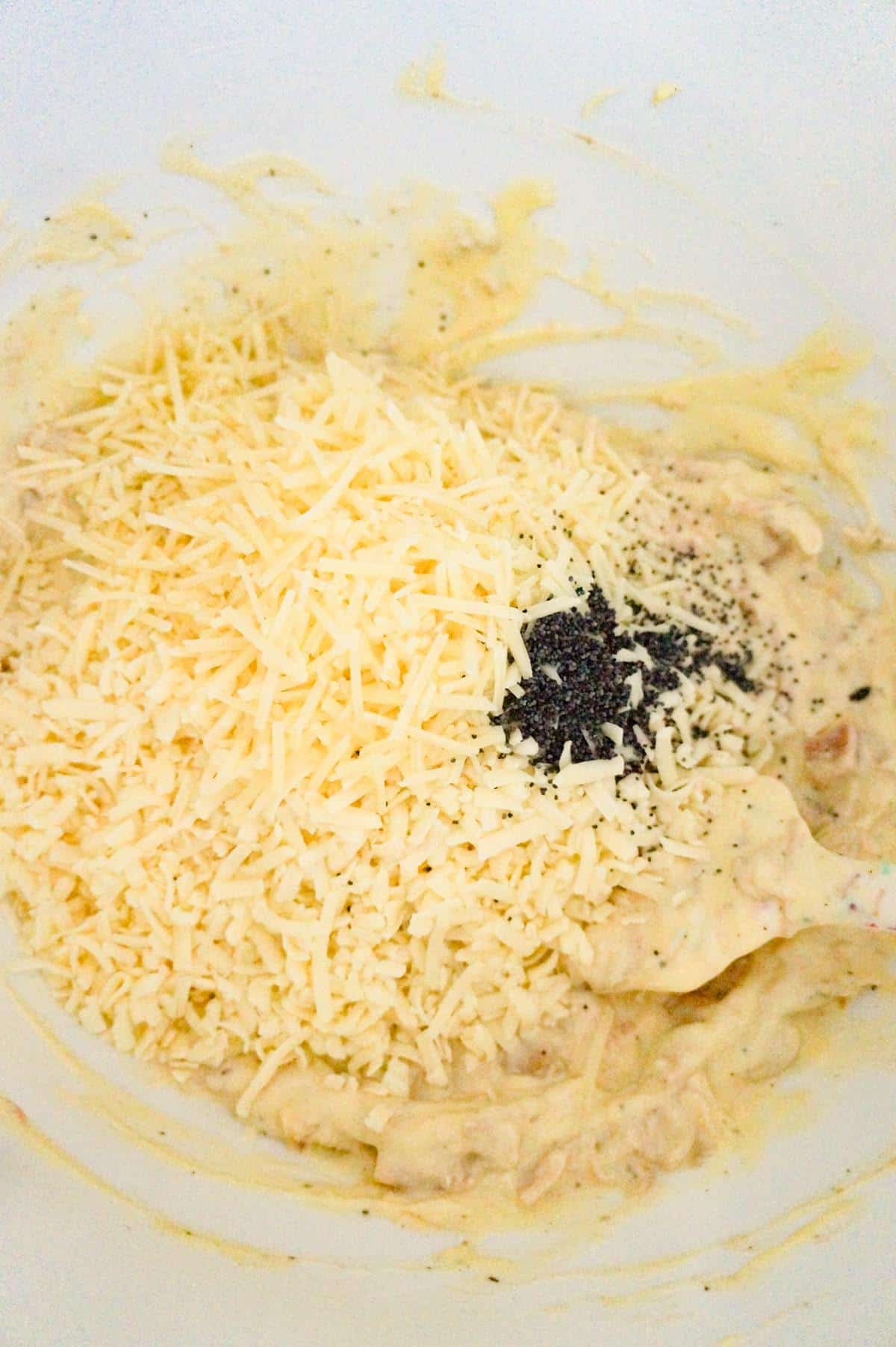 poppy seeds and shredded cheese on top of creamy chicken mixture in a mixing bowl