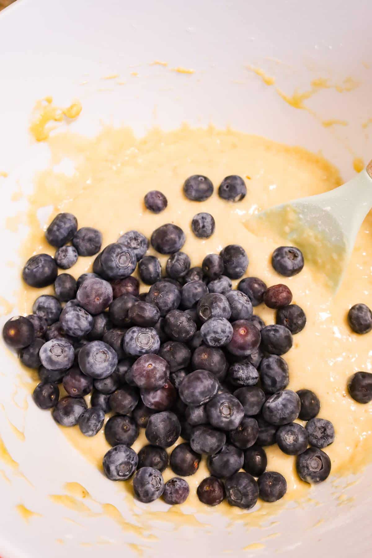 fresh blueberries on top of banana muffin batter in a mixing bowl