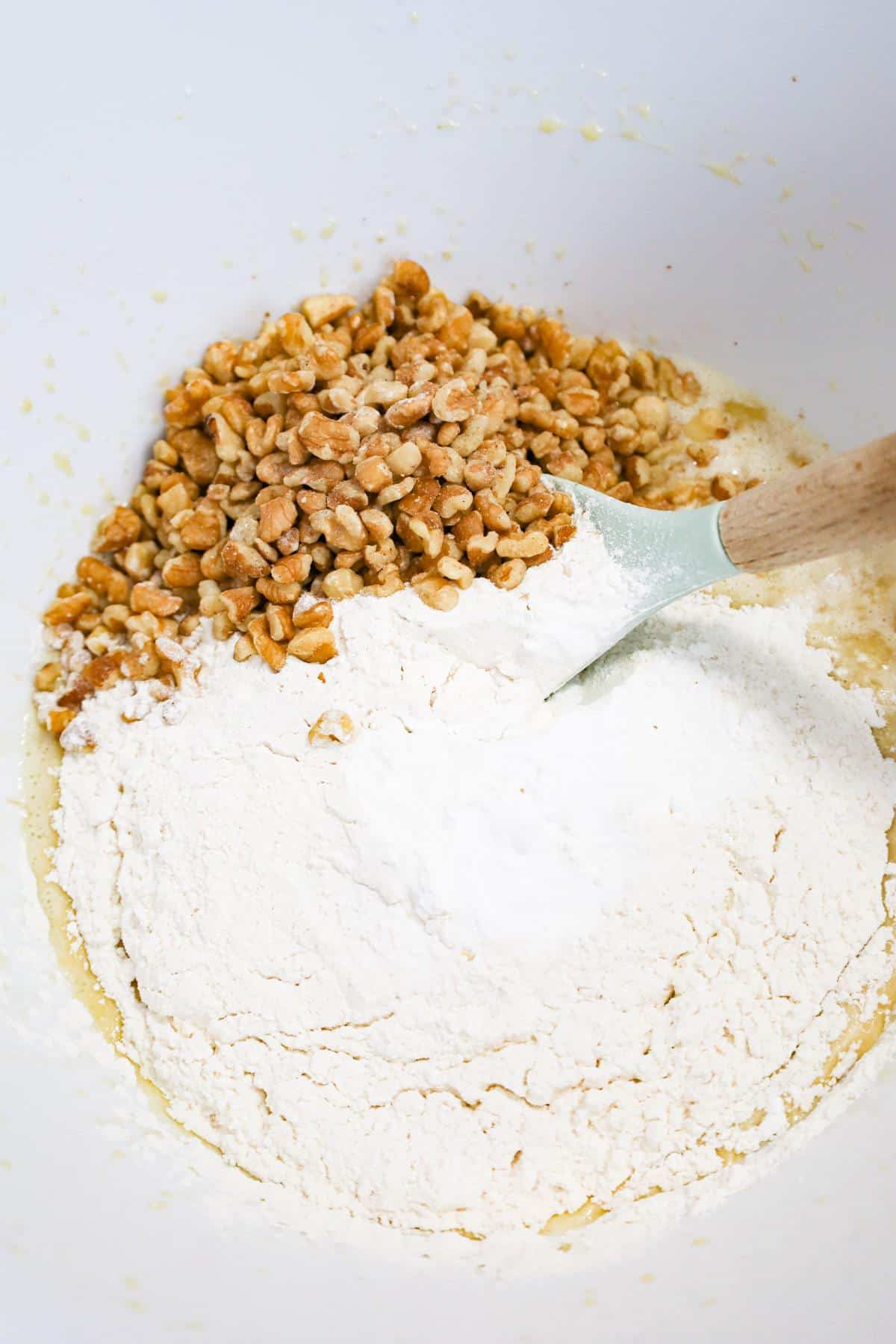 flour and walnuts on top of banana muffin batter in a mixing bowl
