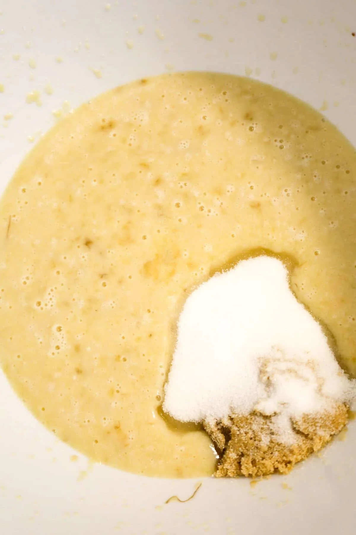 granulated sugar and light brown sugar on top of a creamy banana mixture in a mixing bowl