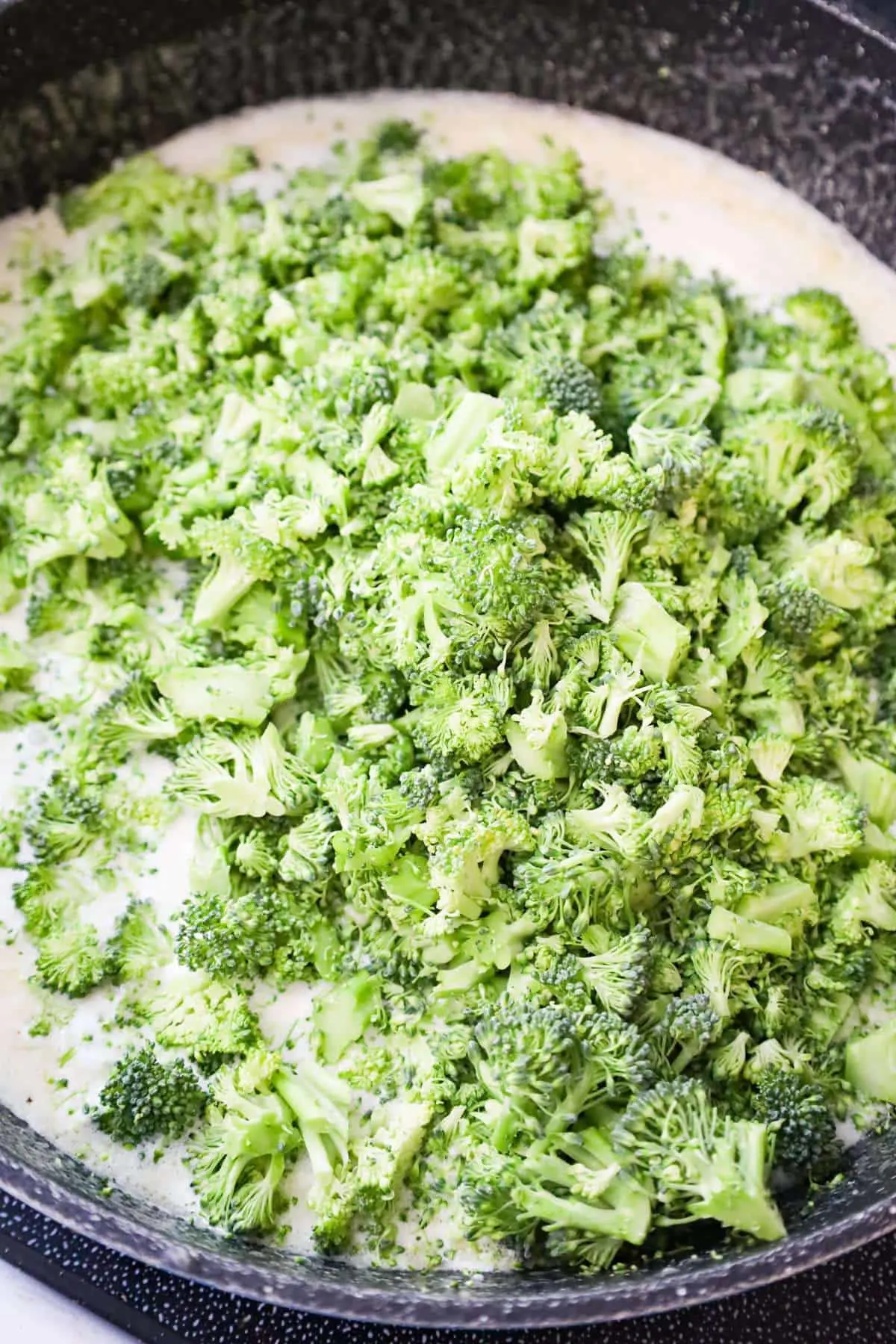 chopped broccoli florets on top of a cream sauce in a saute pan
