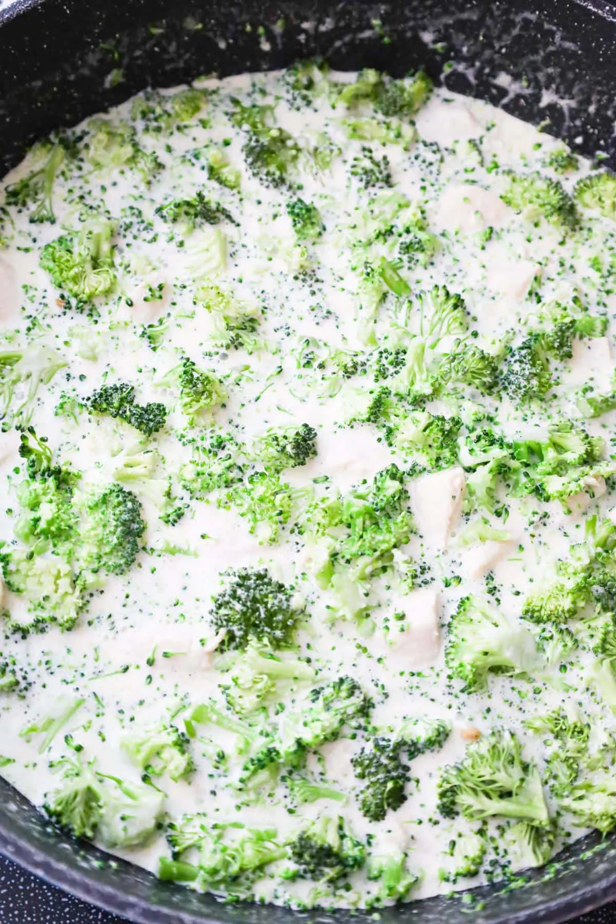 chopped broccoli florets stirred into cream sauce in sauce pan