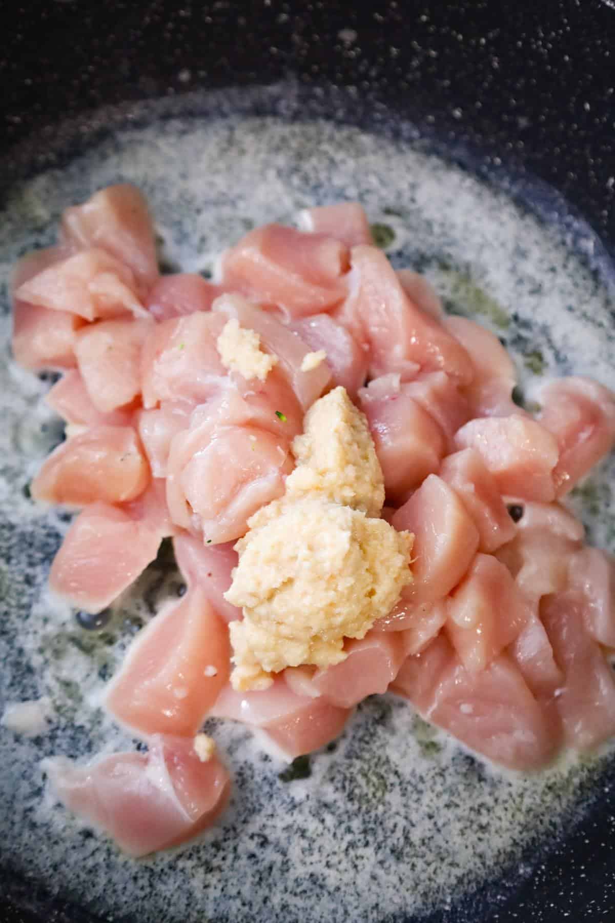 garlic puree on top of raw chicken breast chunks in a saute pan