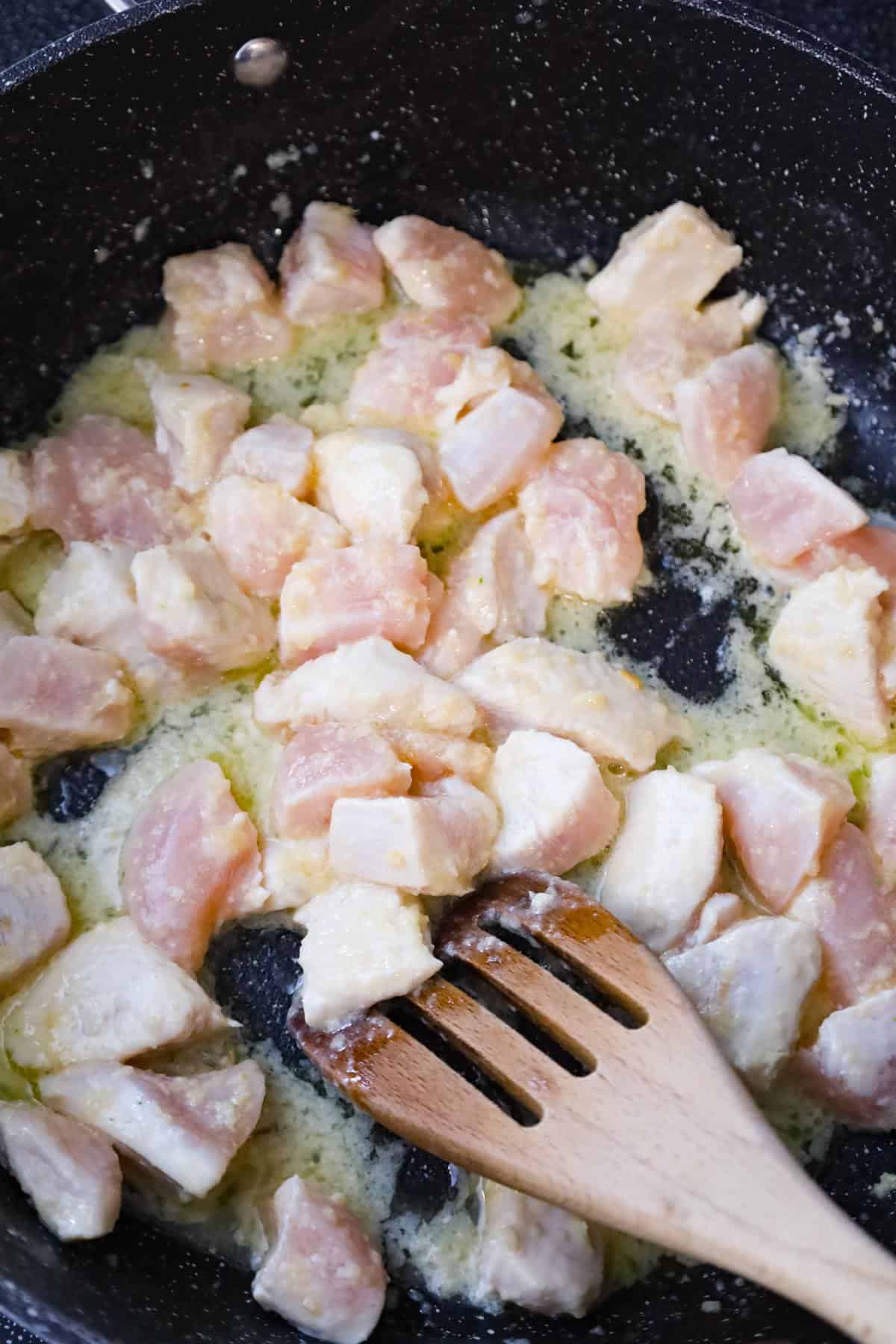 raw chicken breast chunks cooking in butter in a saute pan