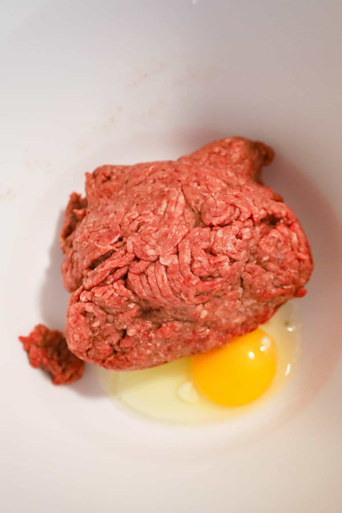 raw ground beef and an egg in a mixing bowl