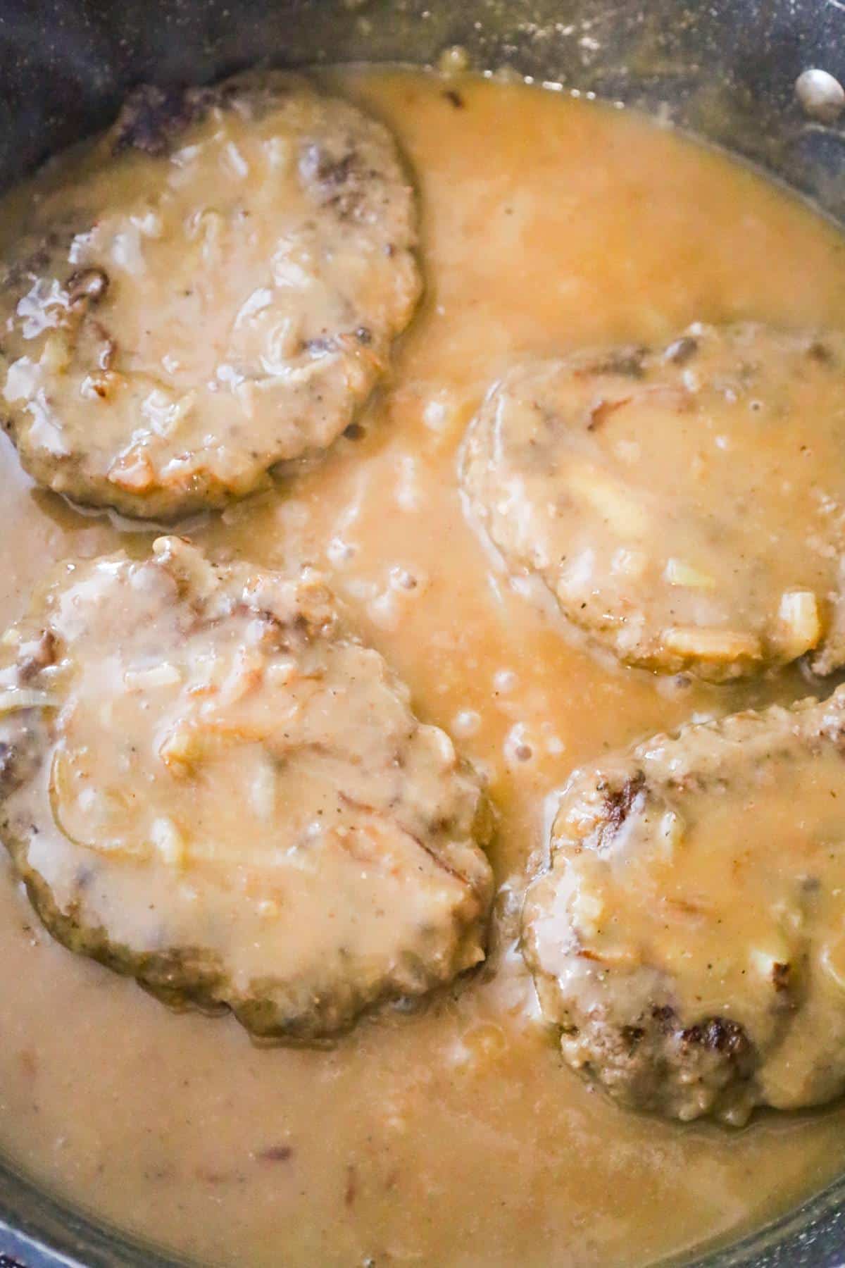 gravy on top of hamburger steaks in a pan