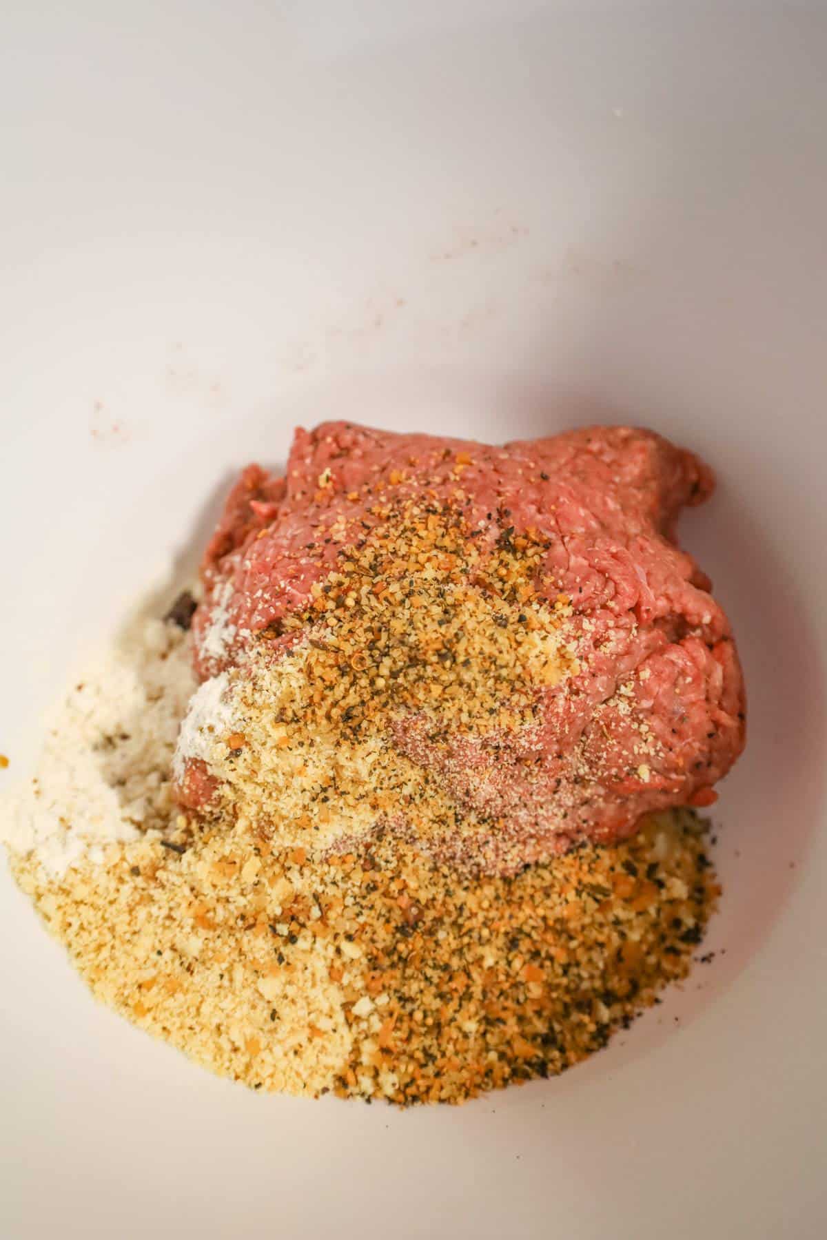 Ritz cracker crumbs and steak spice on top of raw ground beef in a mixing bowl