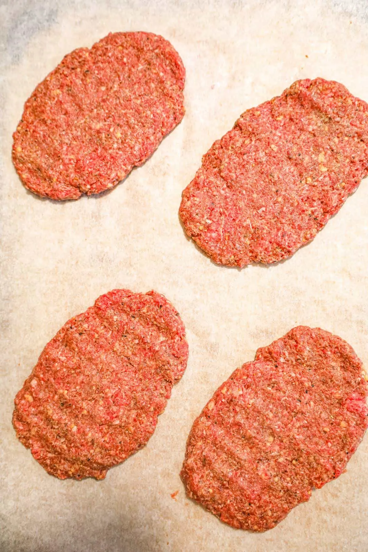 raw hamburger patties on parchment paper