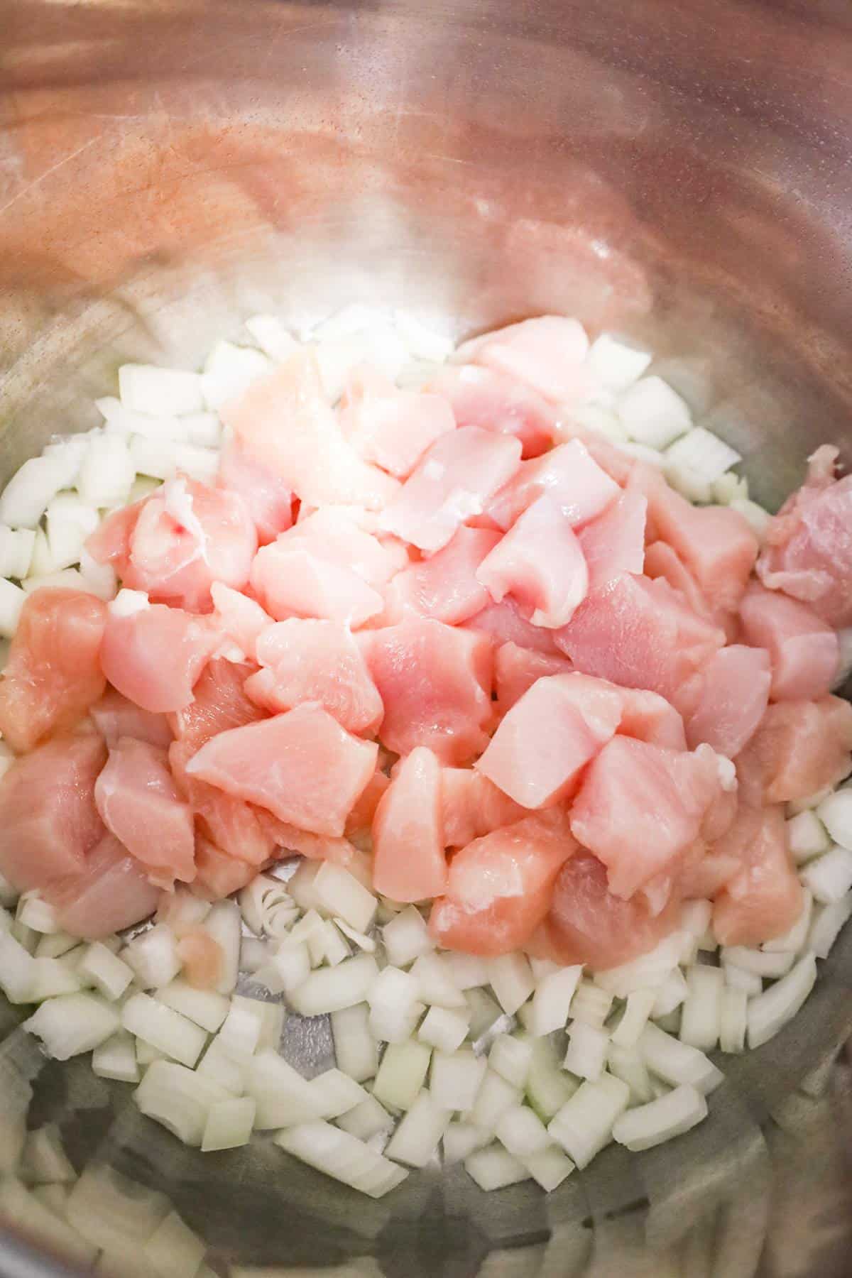 raw chicken breast chunks and diced yellow onions in an Instant Pot