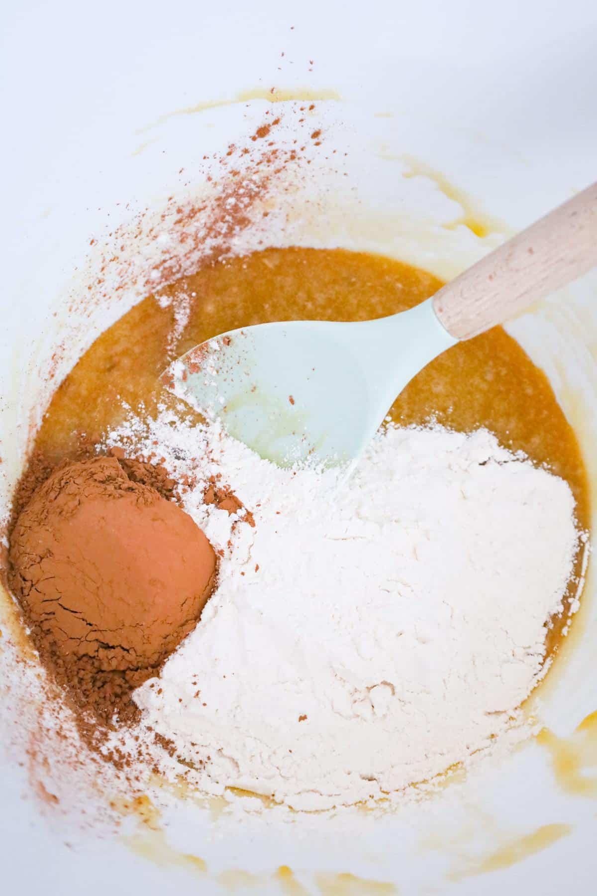 cocoa powder and all purpose flour on top of sugar, egg and butter mixture in a mixing bowl
