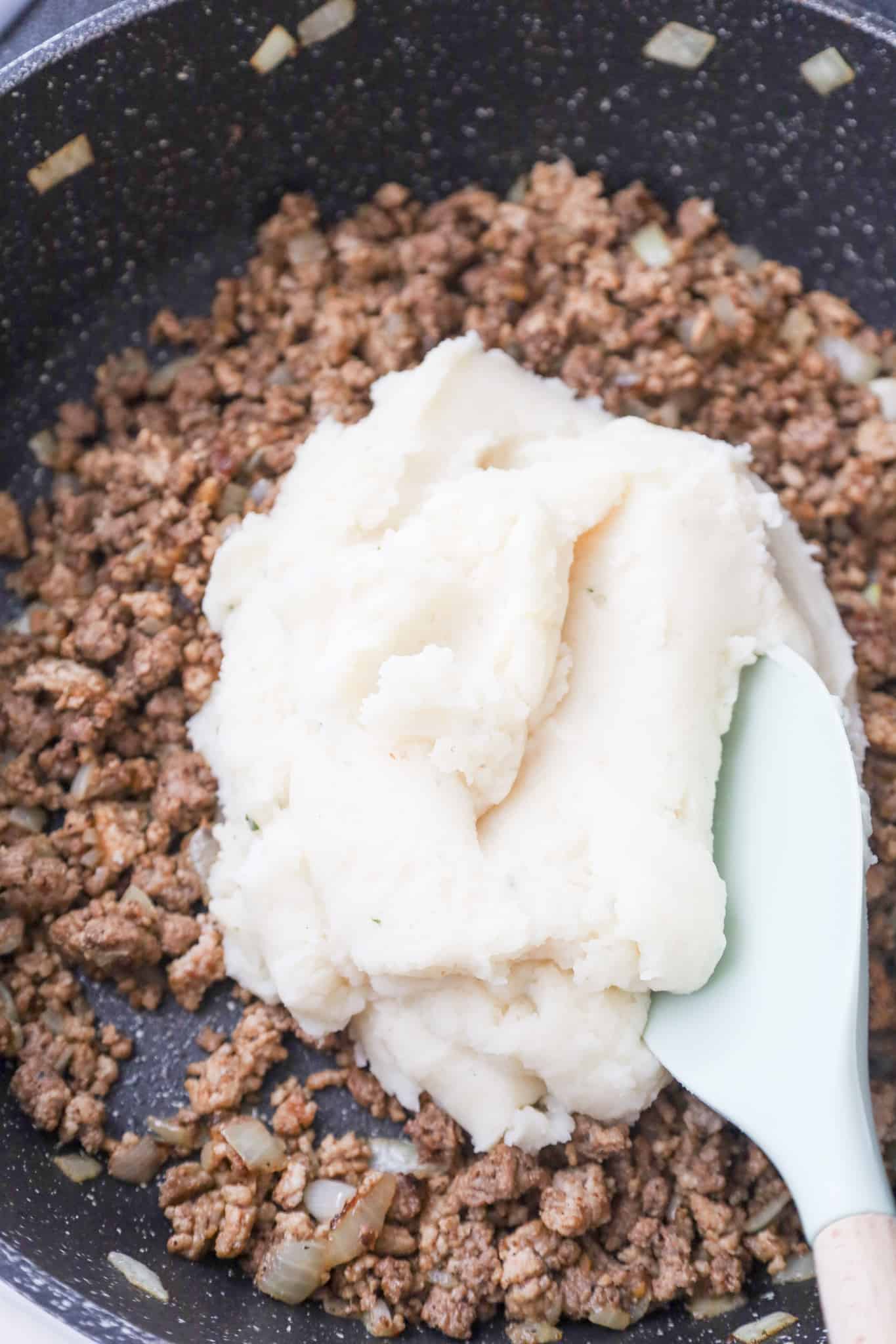 mashed potatoes on top of cooked ground beef and ground pork mixture in a saute pan