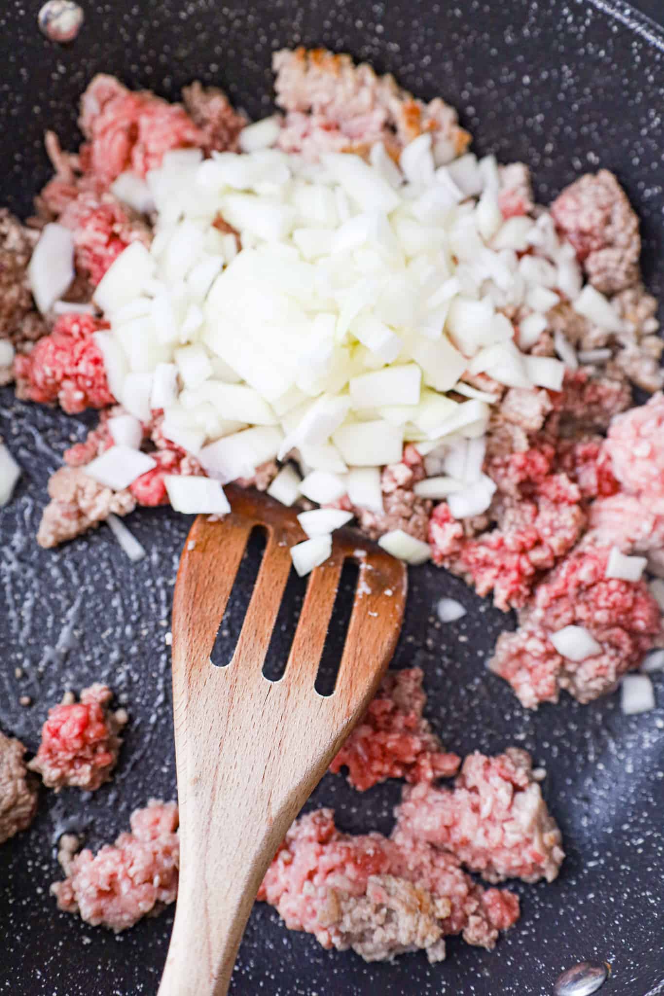 diced onions on top of ground beef and ground pork cooking in a saute pan