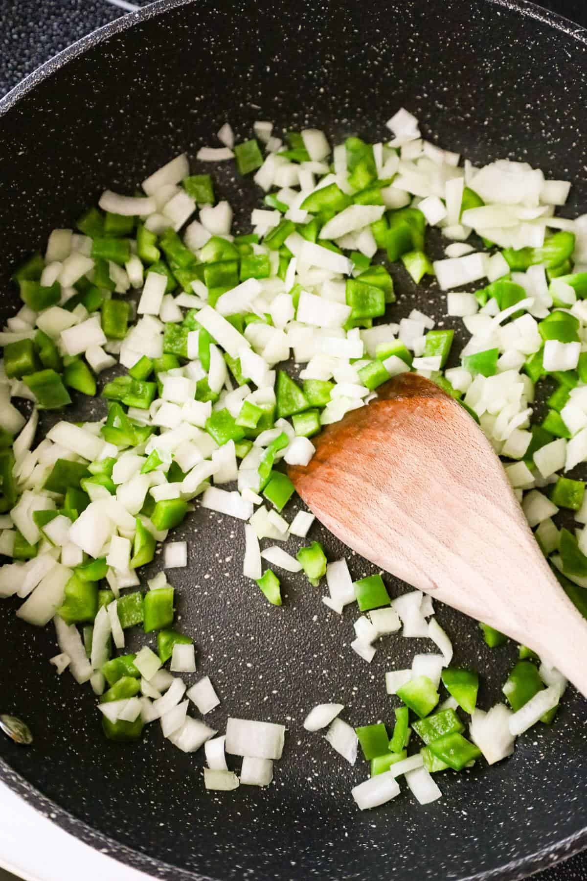 diced green peppers and onions being stirred in a saute pan