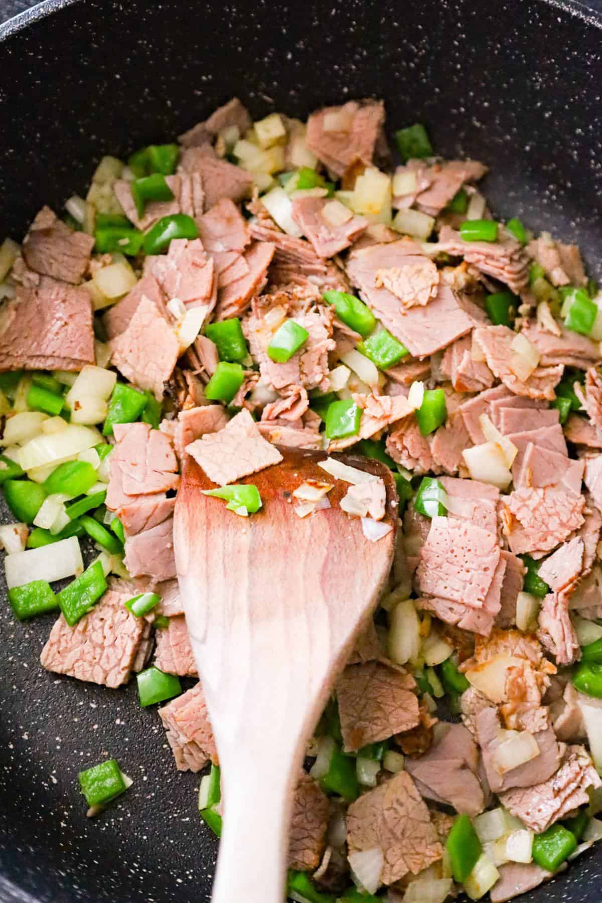 chopped roast beef, diced green peppers and onions being stirred in a saute pan