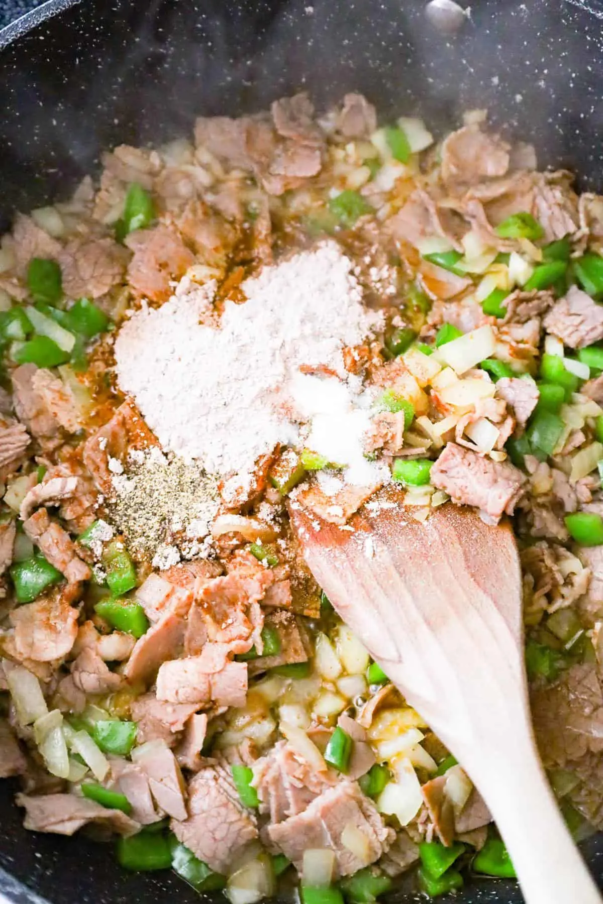 brown gravy mixing on top of chopped roast beef, green peppers and onions in a saute pan