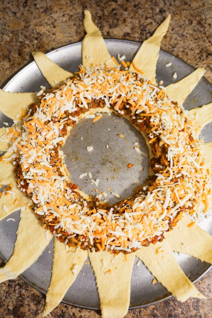 shredded cheese on top of ground beef mixture on crescent dough ring