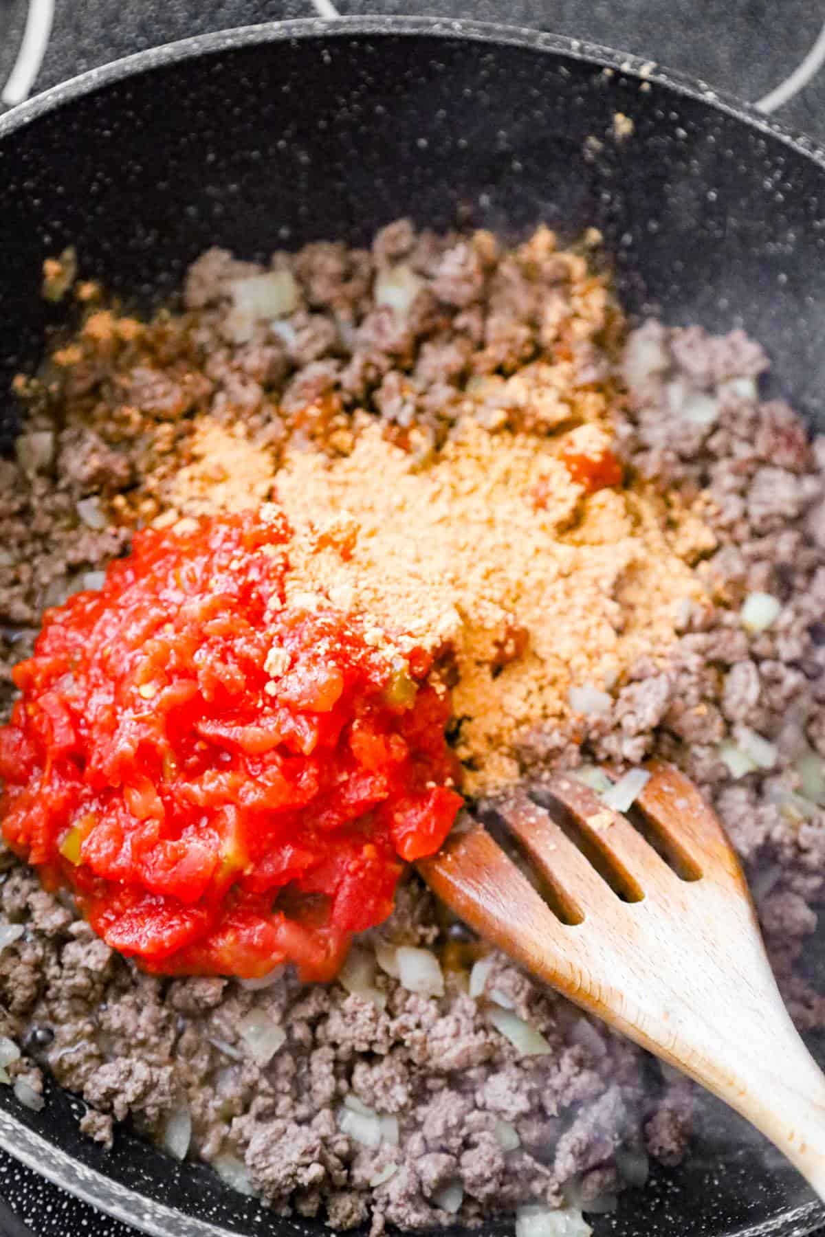 Rotel and taco seasoning on top of cooked ground beef in a saute pan