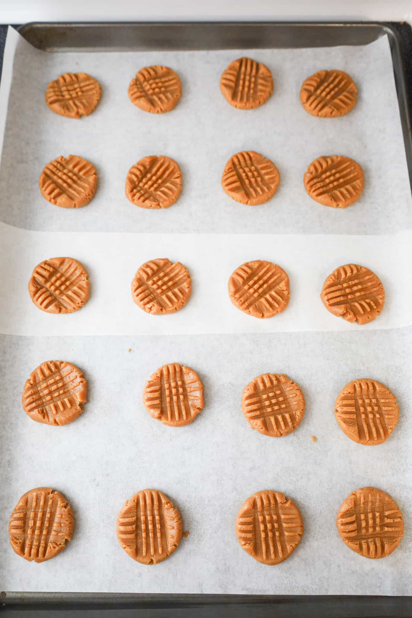 flattened peanut butter cookie dough balls on a parchment lined baking sheet