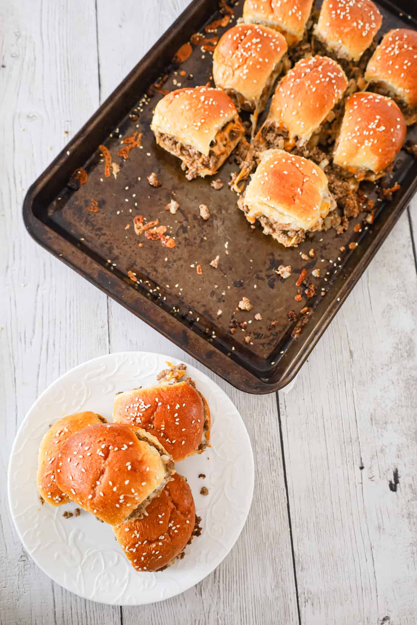 Cheeseburger Sliders are mini sandwiches made with crumbled ground beef and diced onions tossed in ketchup, mayo and mustard all loaded onto dinner rolls and topped with shredded cheese.