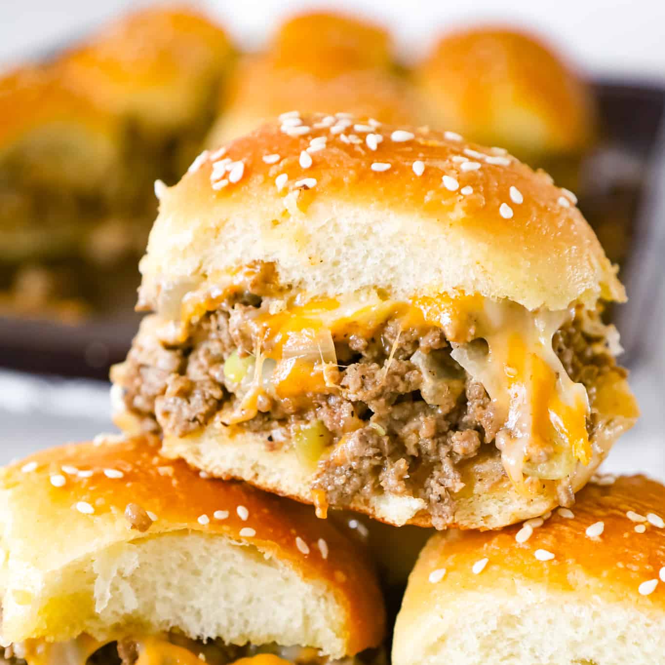 Cheeseburger Sliders are mini sandwiches made with crumbled ground beef and diced onions tossed in ketchup, mayo and mustard all loaded onto dinner rolls and topped with shredded cheese.