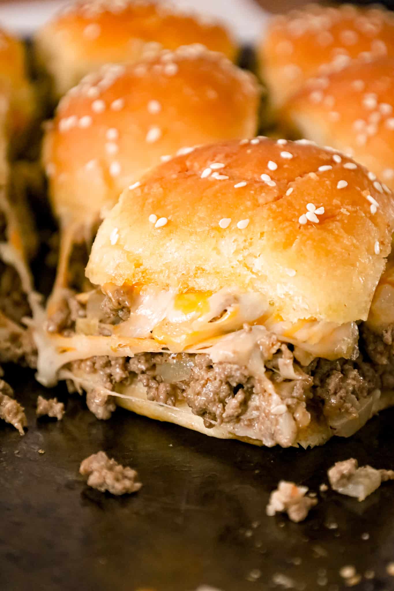 Cheeseburger Sliders are mini sandwiches made with crumbled ground beef and diced onions tossed in ketchup, mayo and mustard all loaded onto dinner rolls and topped with shredded cheese.