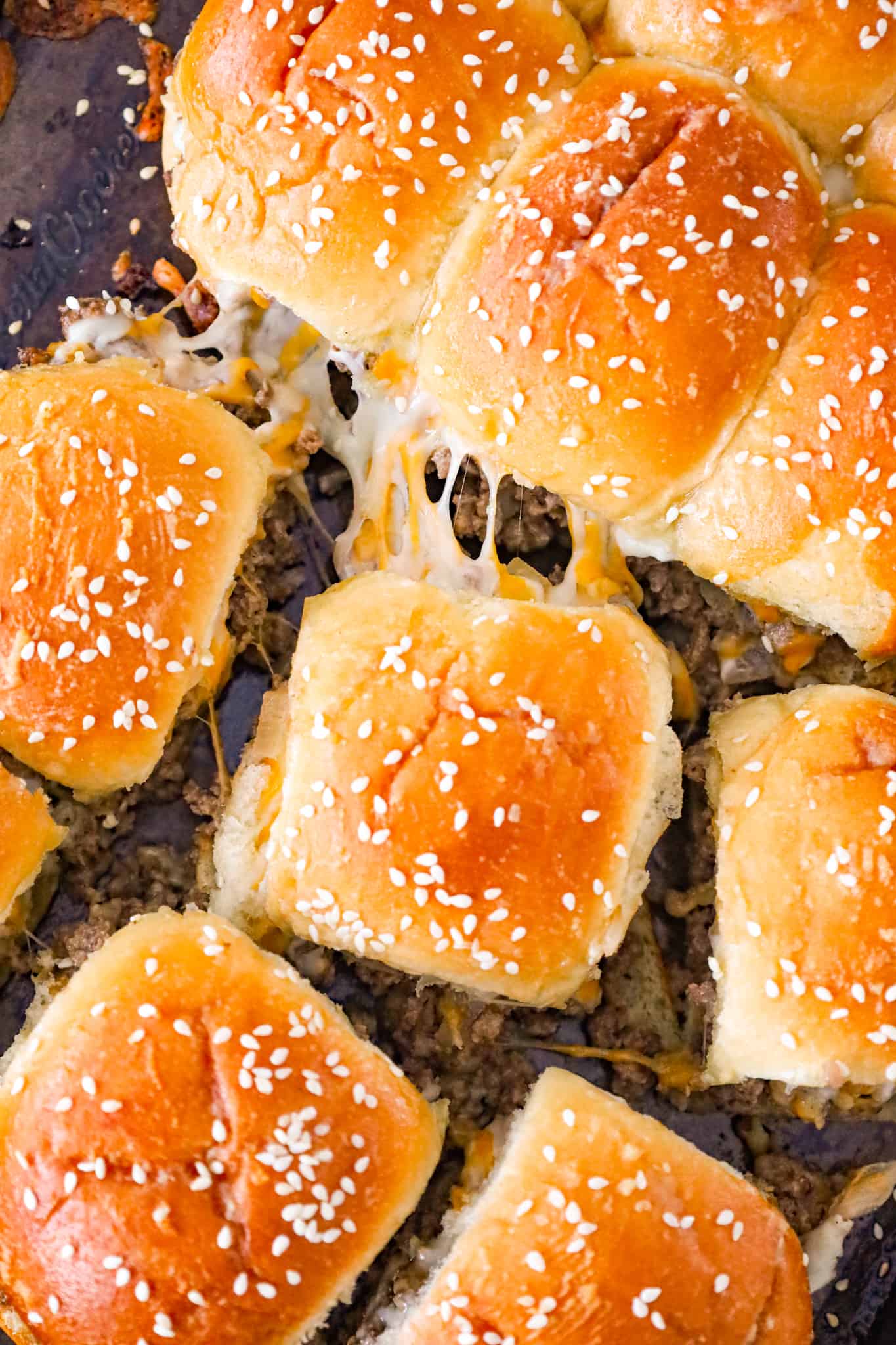 Cheeseburger Sliders are mini sandwiches made with crumbled ground beef and diced onions tossed in ketchup, mayo and mustard all loaded onto dinner rolls and topped with shredded cheese.