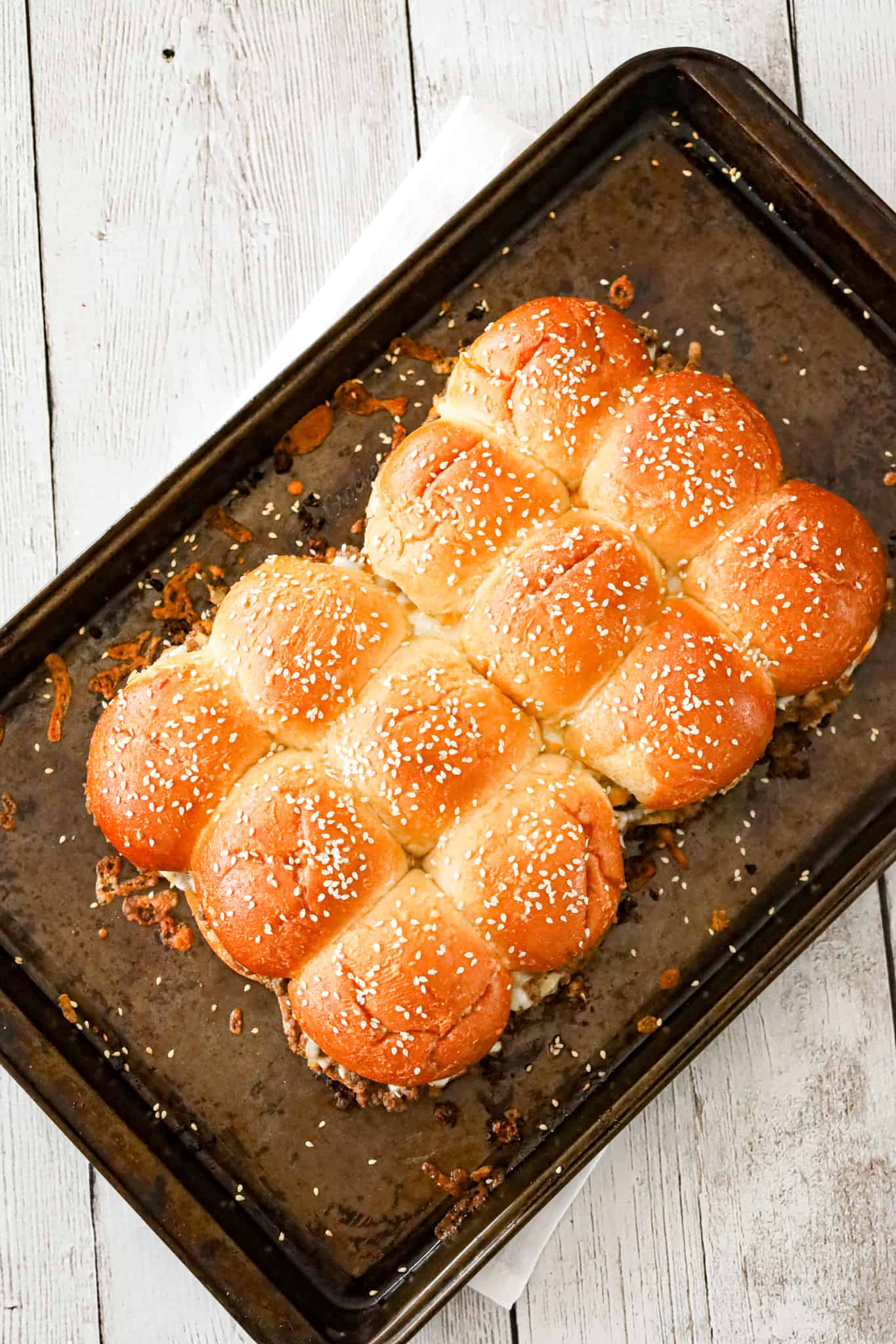 Cheeseburger Sliders are mini sandwiches made with crumbled ground beef and diced onions tossed in ketchup, mayo and mustard all loaded onto dinner rolls and topped with shredded cheese.