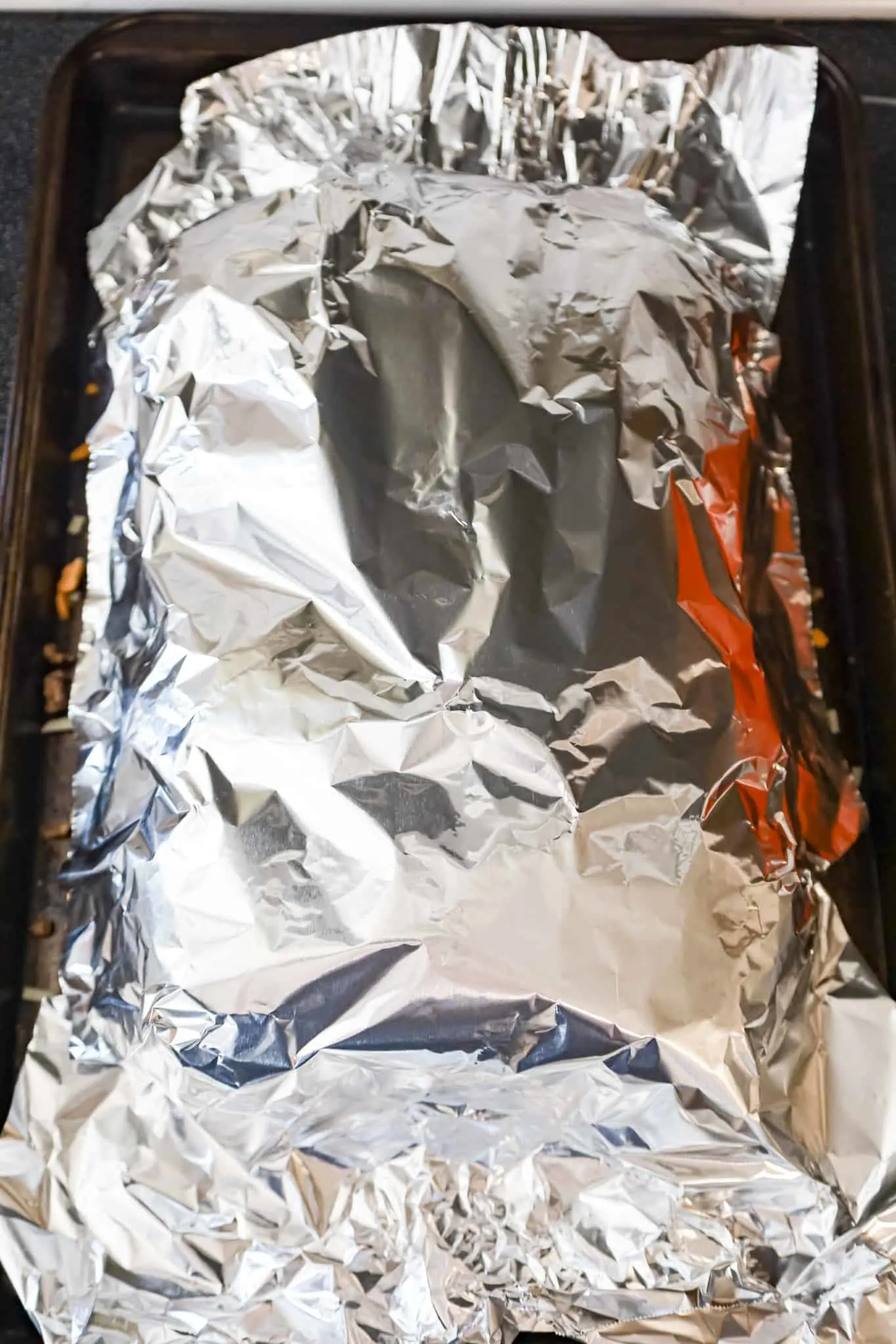 aluminum foil over sliders on a baking sheet