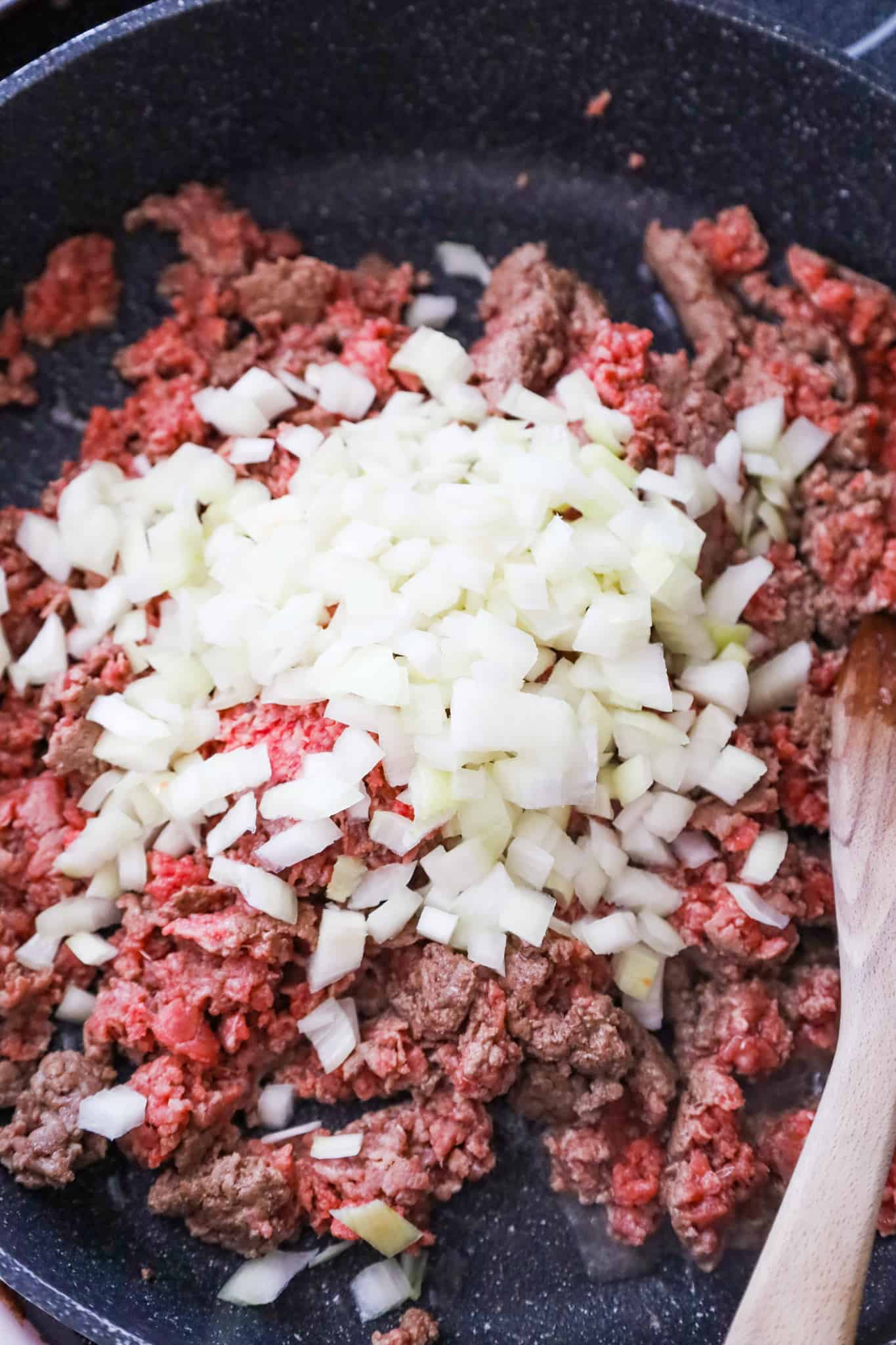 diced onions on top of raw ground beef in a saute pan