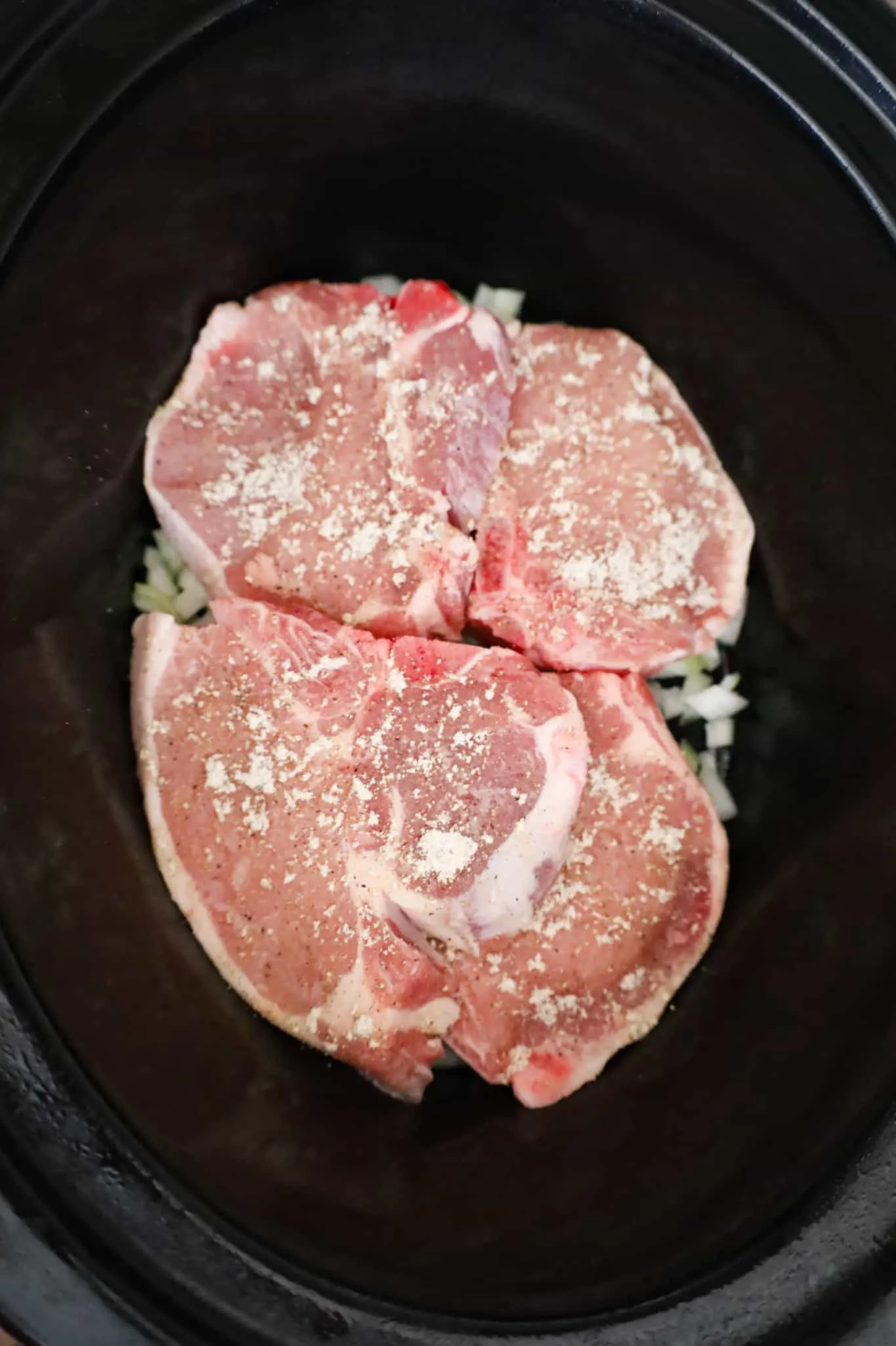 raw pork chops on top of diced onions in a crock pot