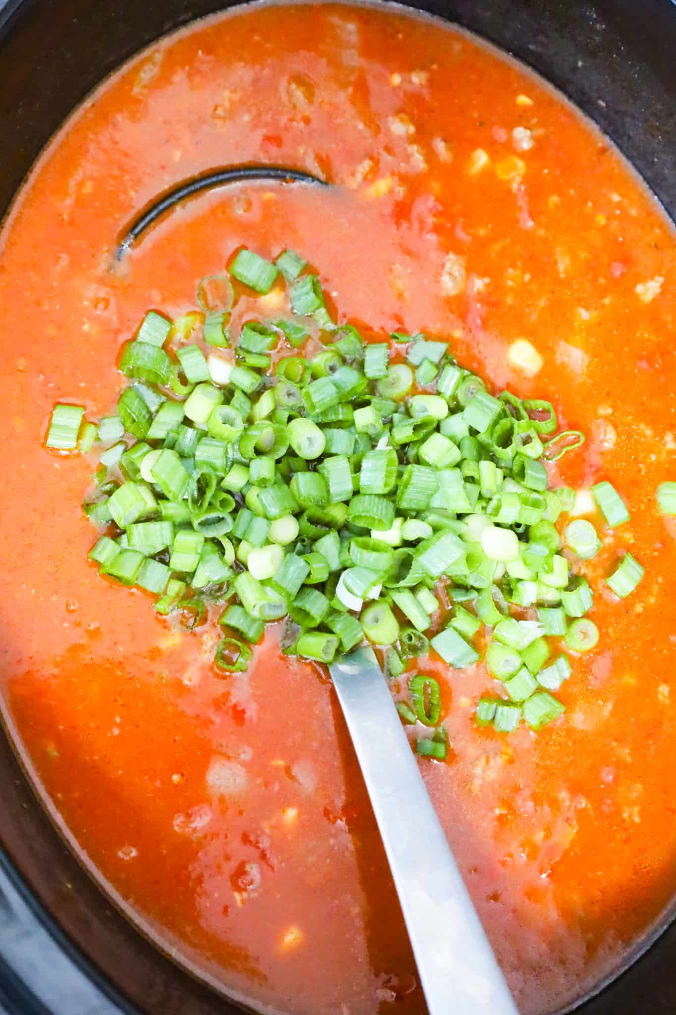 chopped green onions on top of beef taco soup in a slow cooker