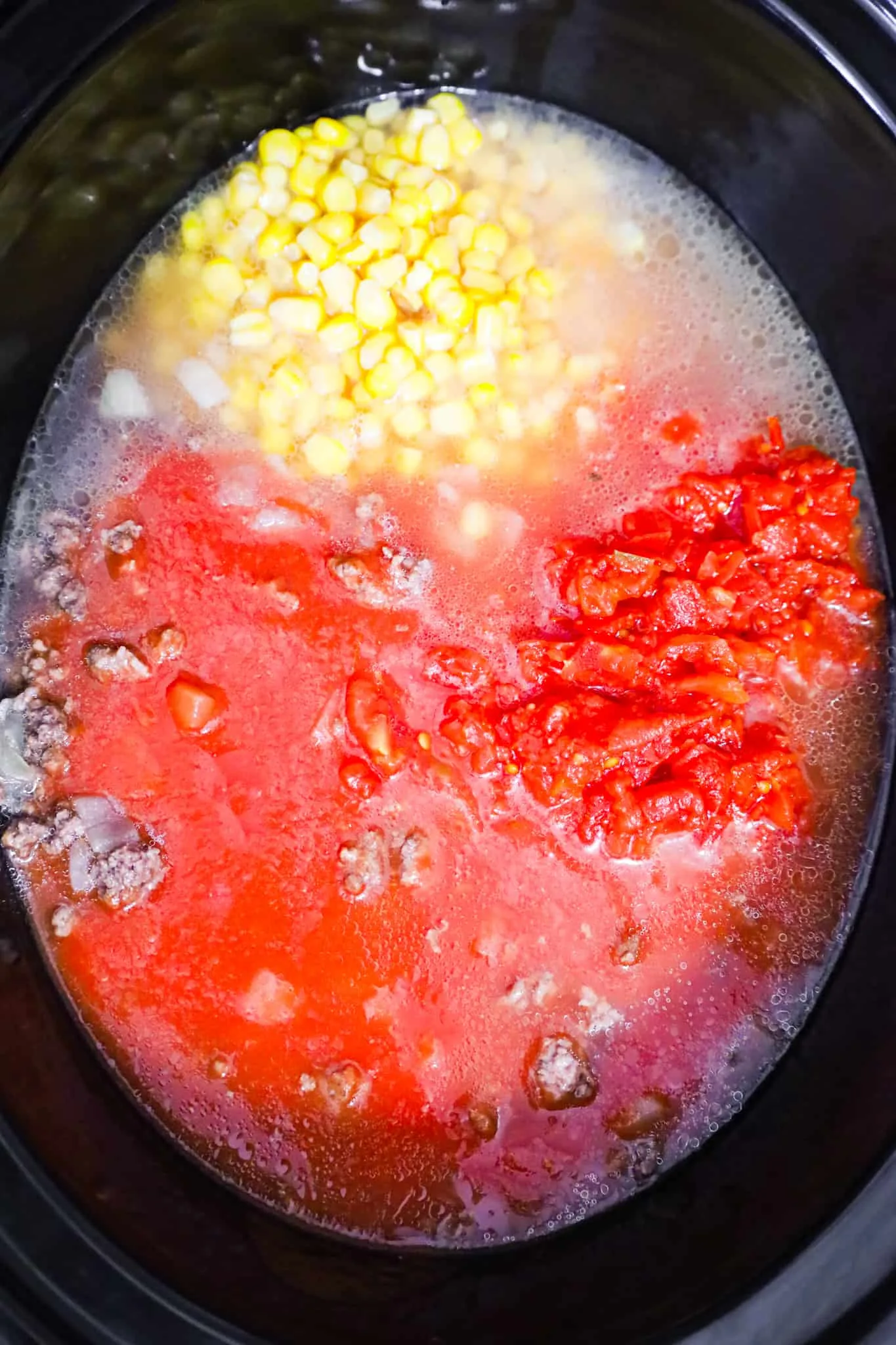 corn, Rotel diced tomatoes and tomato sauce on top of ground beef in a crock pot