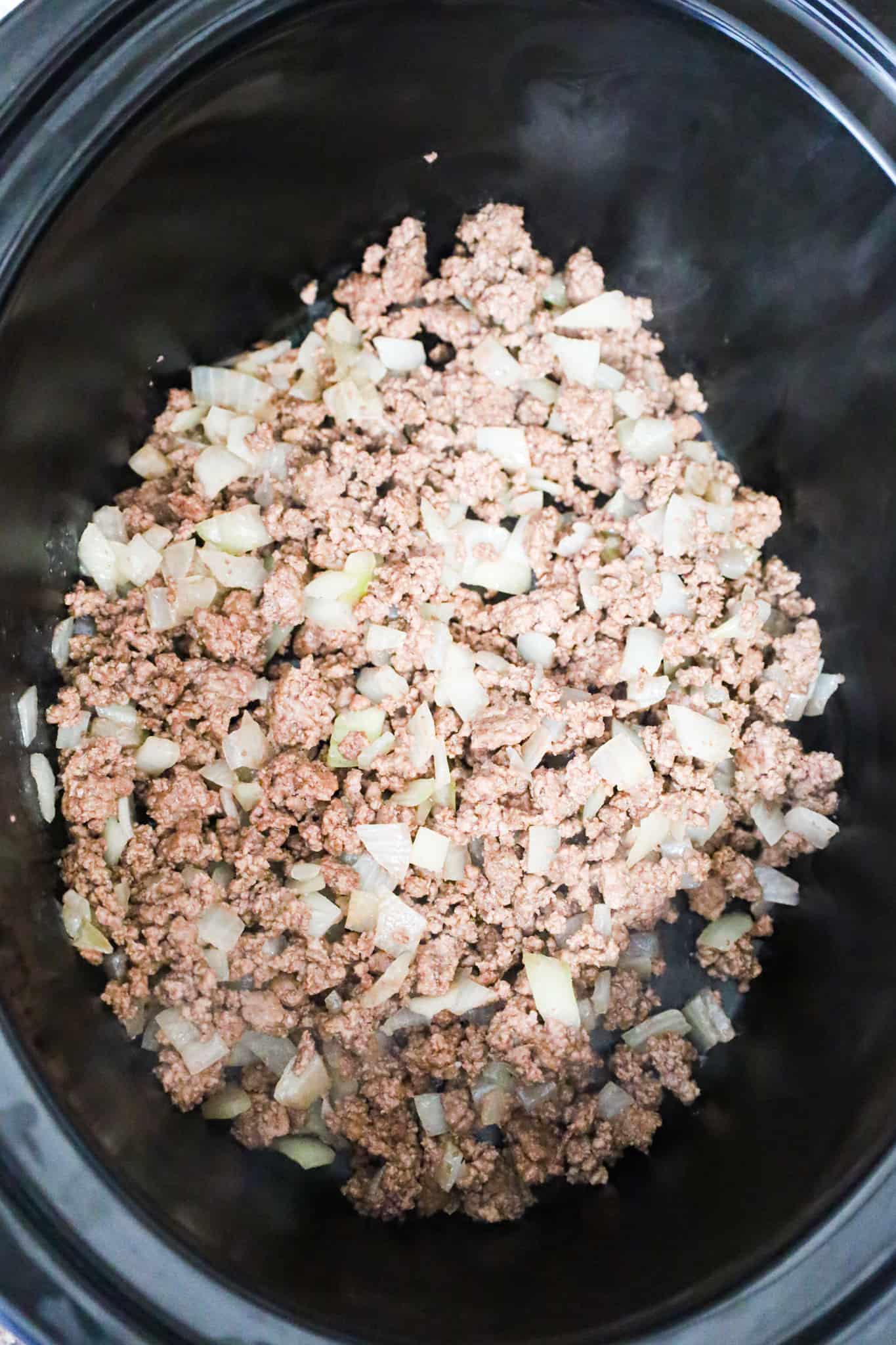 crumbled ground beef and diced onions in the bottom of a crock pot
