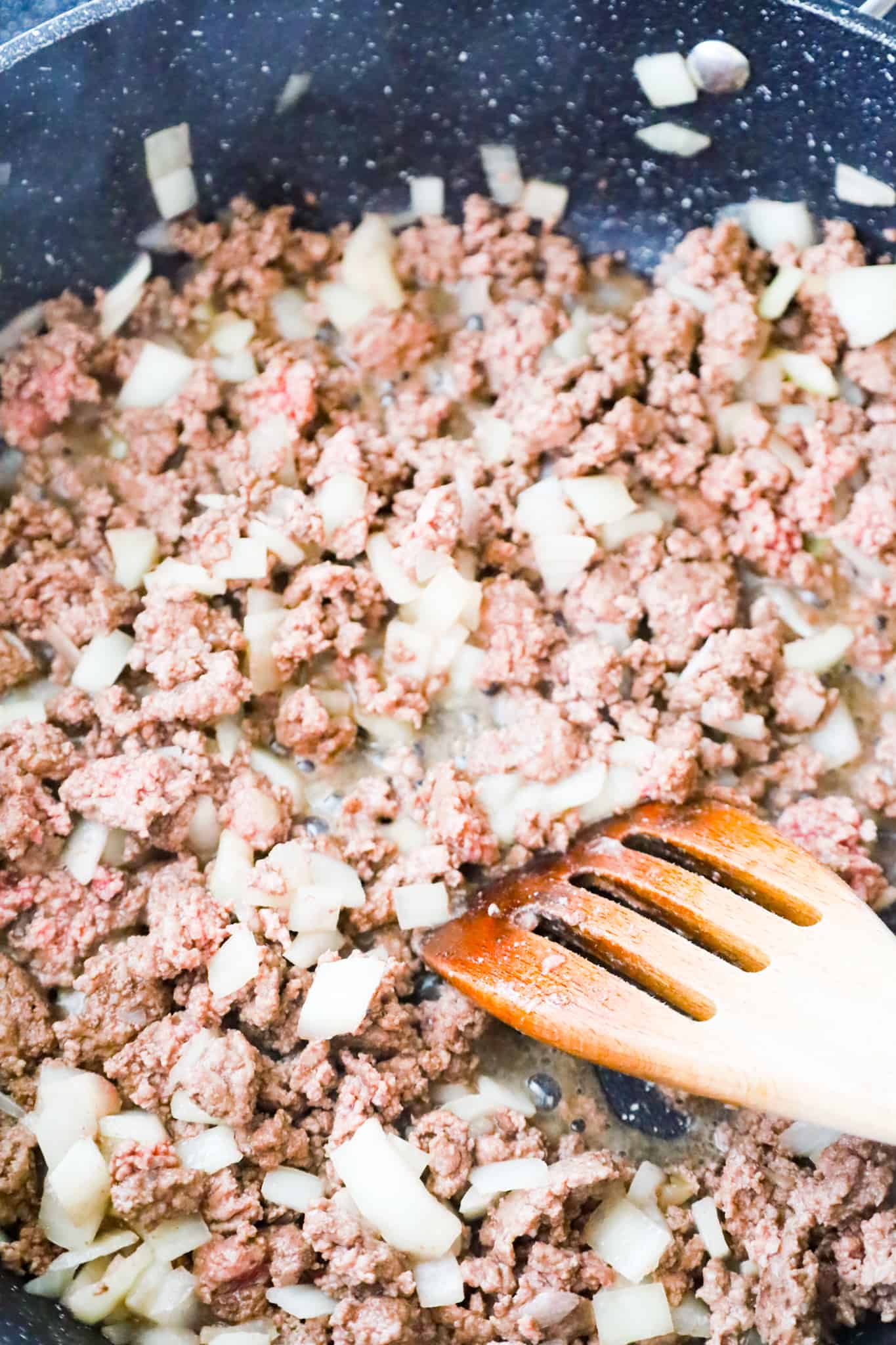 crumbled ground beef and diced onions cooking in a saute pan